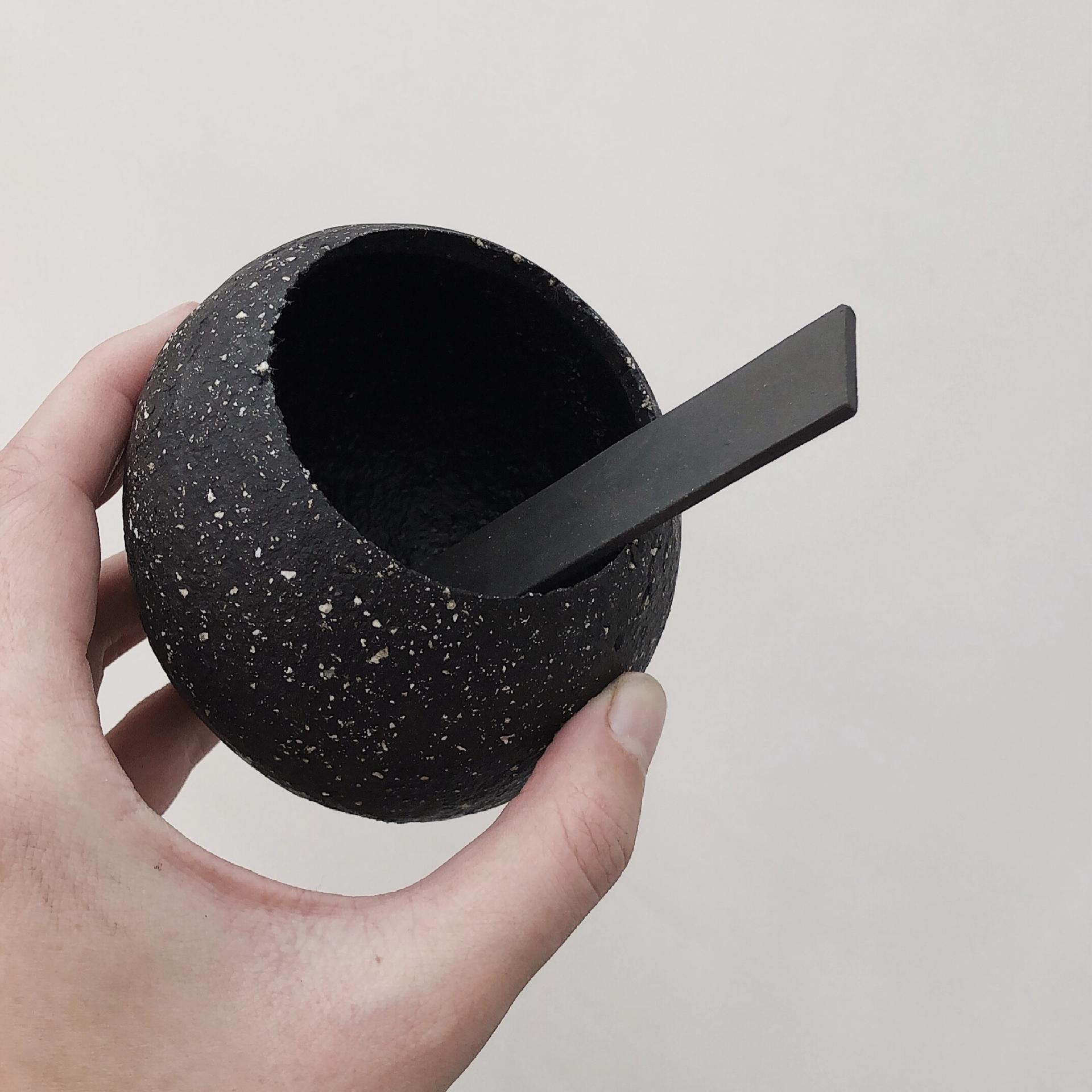 Ceramic artist Sophie Farrar holds a unique, textured black bowl with a flat black ceramic spoon inside.