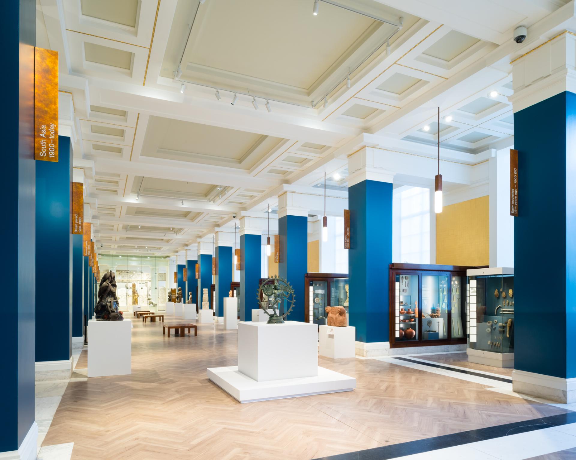 Exhibition hall showcasing sculptures and artifacts in a modern museum with vibrant blue walls and elegant architectural design.