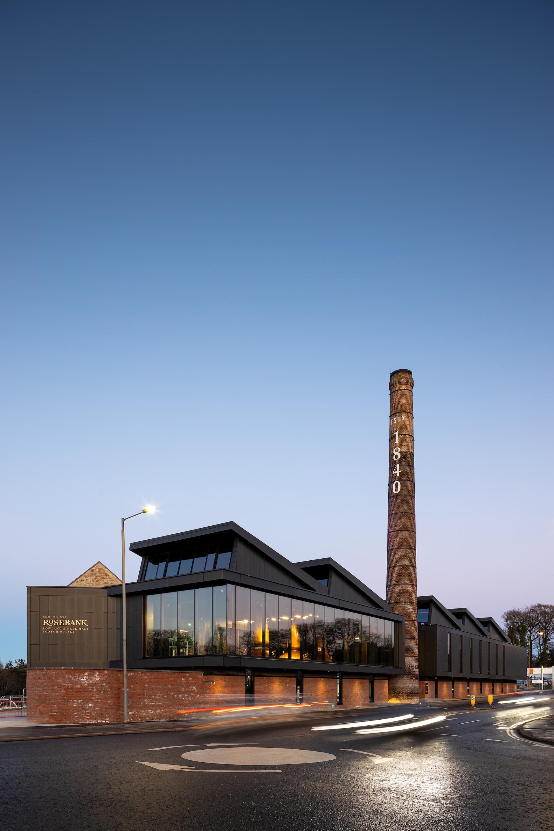 Historic Rosebank Distillery features modern architecture alongside a restored chimney, blending tradition with contemporary design.