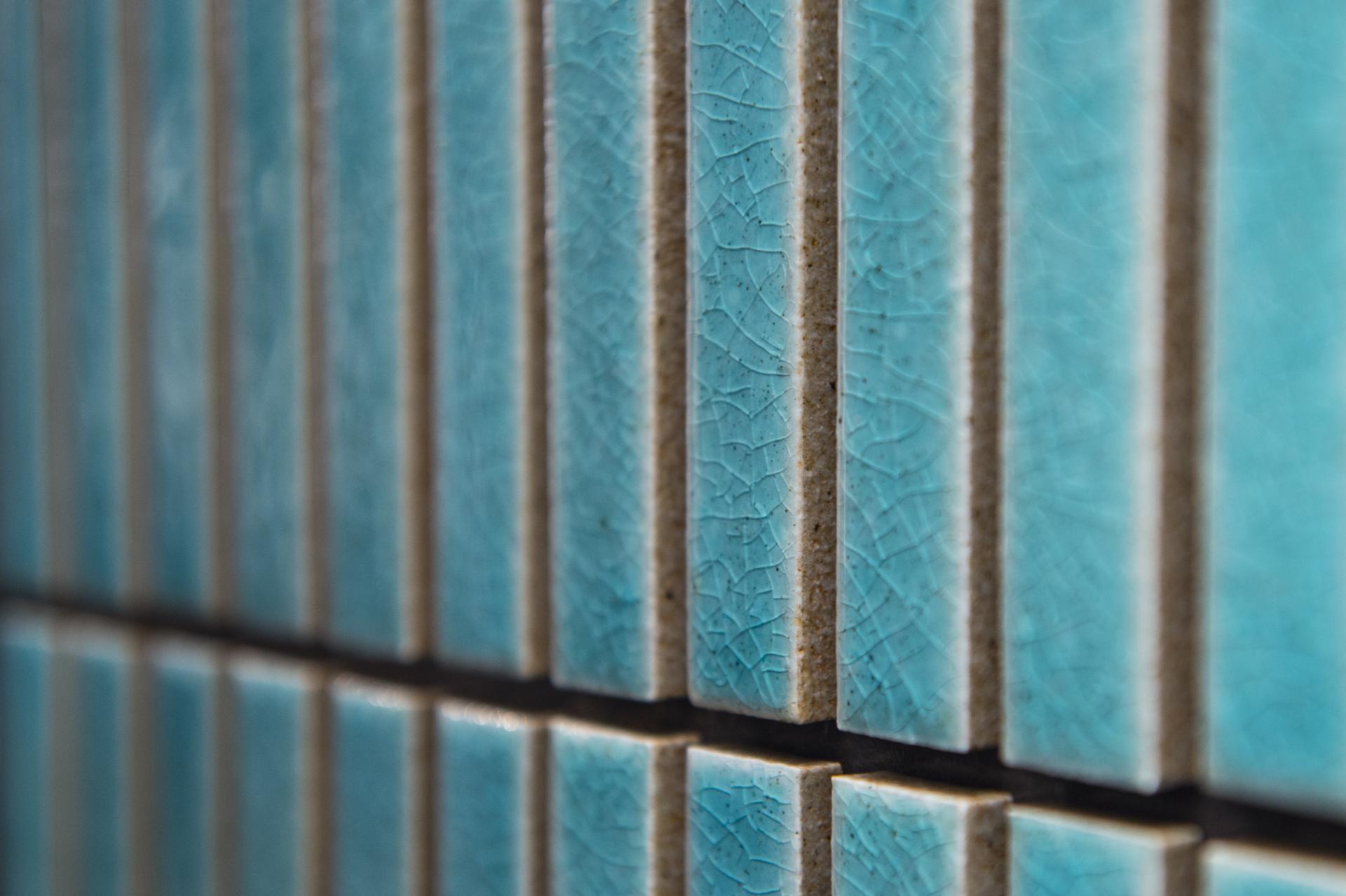 Textured blue ceramic tiles arranged in vertical rows, showcasing unique crackle patterns for the Surface Design Show 2023.