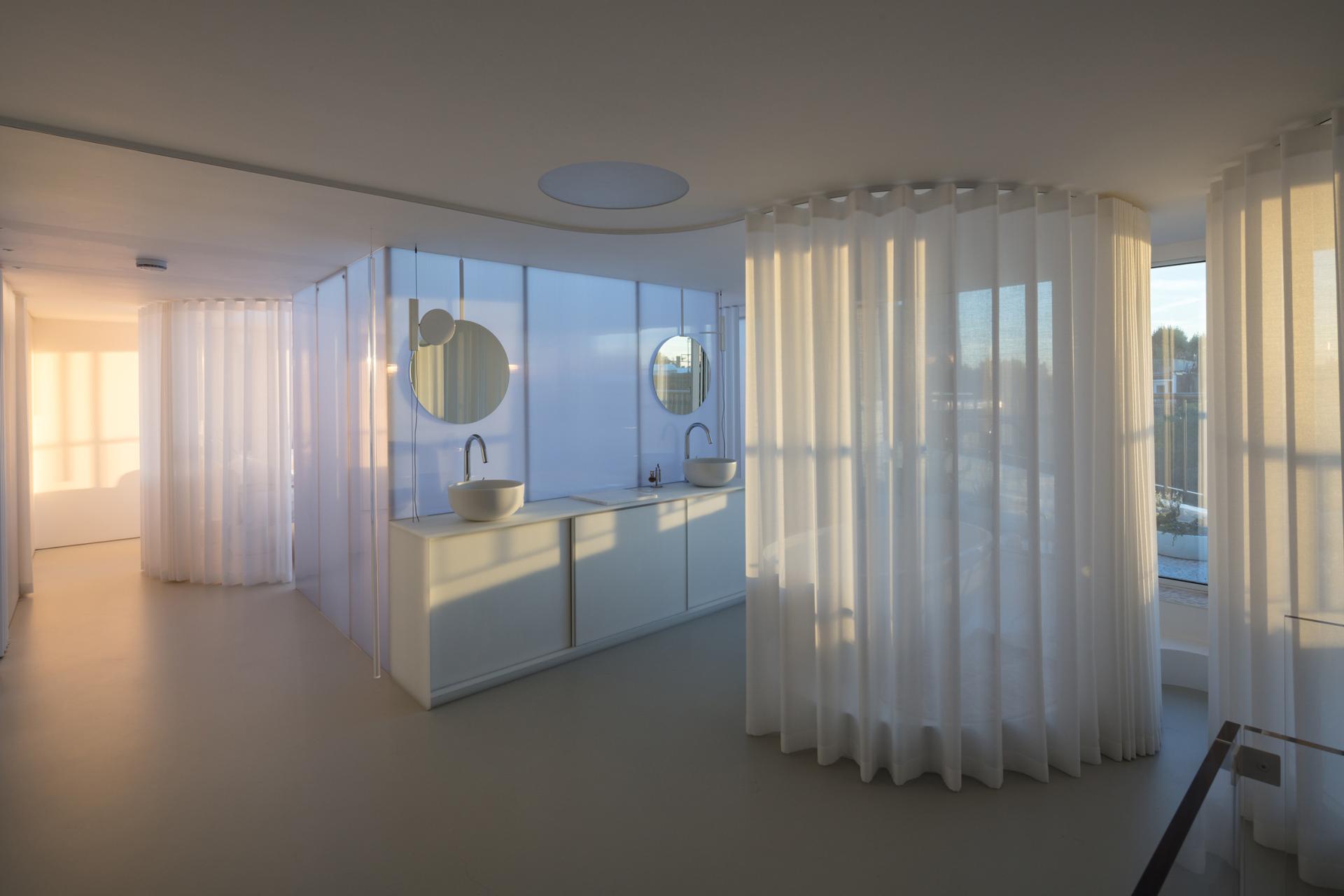 Modern interior of Maggie’s St Barts featuring elegant sinks, circular mirrors, and sheer curtains, showcasing award-winning design.