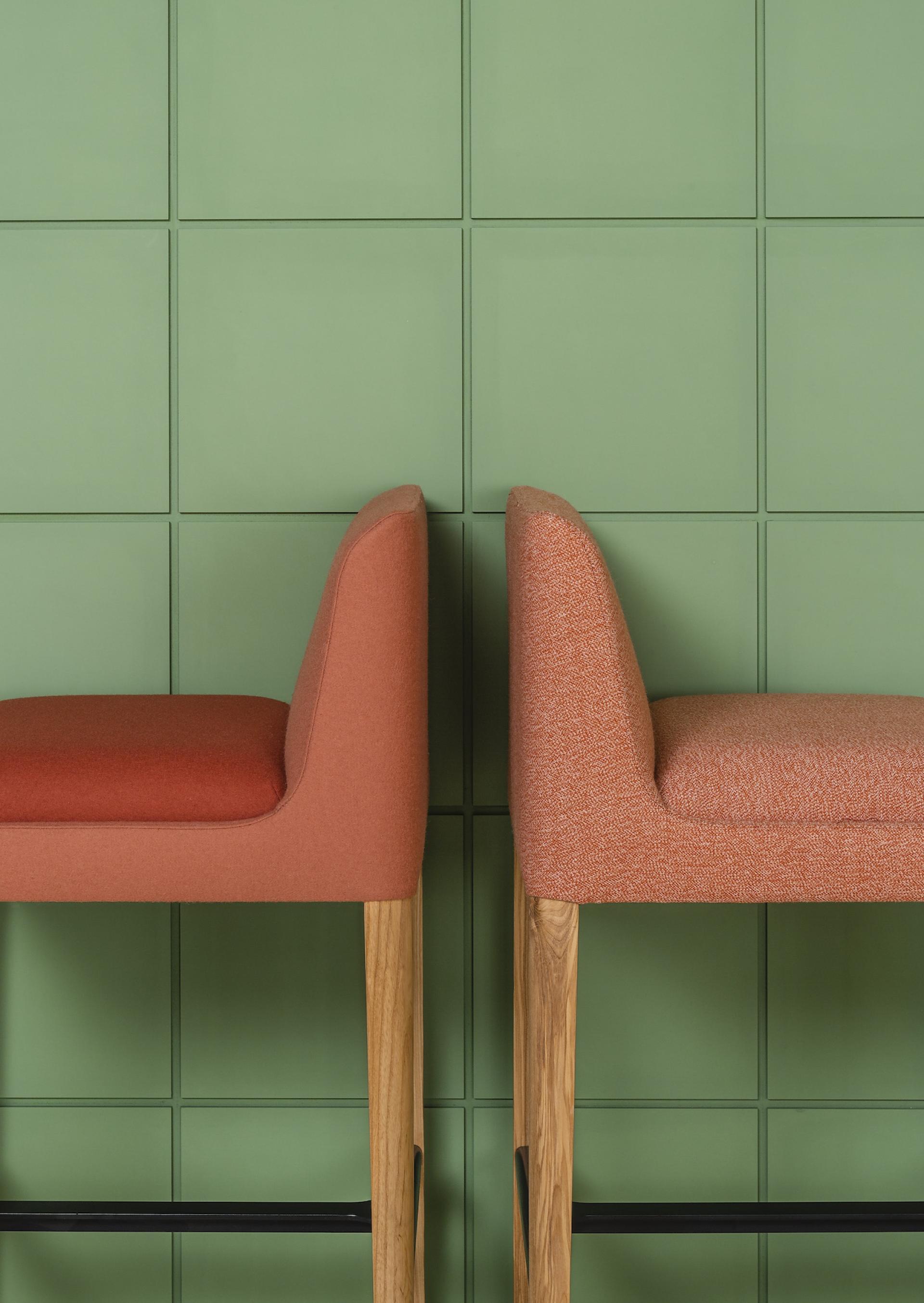 Stylish bar stools in orange fabric against a textured green wall, highlighting contemporary furniture design and comfort.