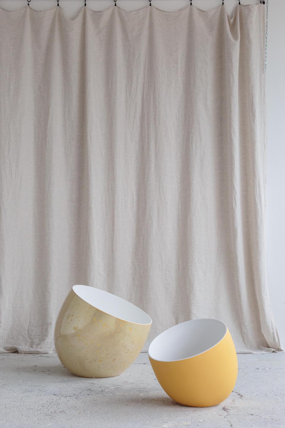 Stylish sculptural bowls in gold and yellow placed against a soft linen backdrop, showcasing modern design from Faïencerie de Charolles.