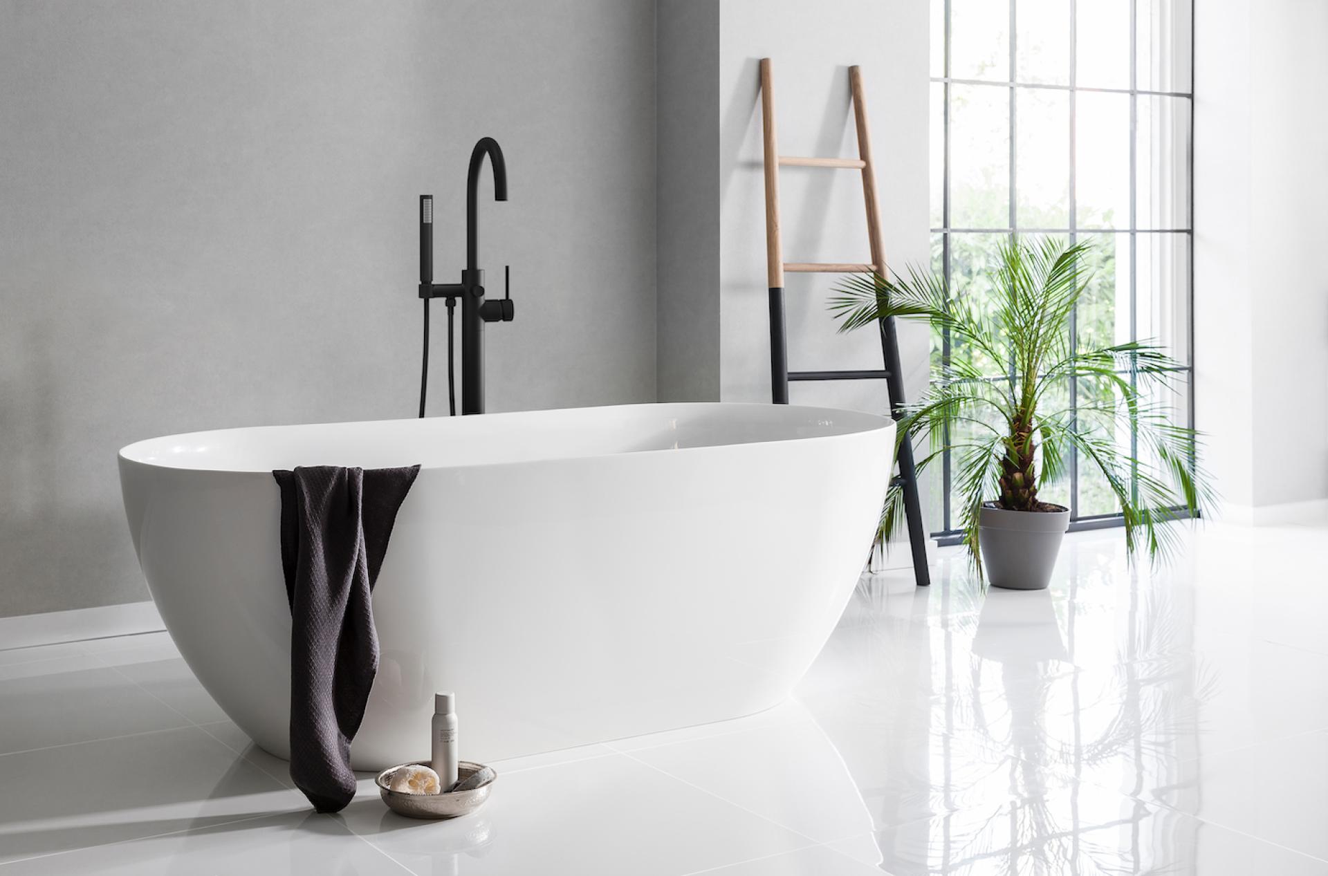 Elegant white freestanding bathtub with black faucet, towel, and indoor plants, showcasing modern bathroom design trends for 2022.