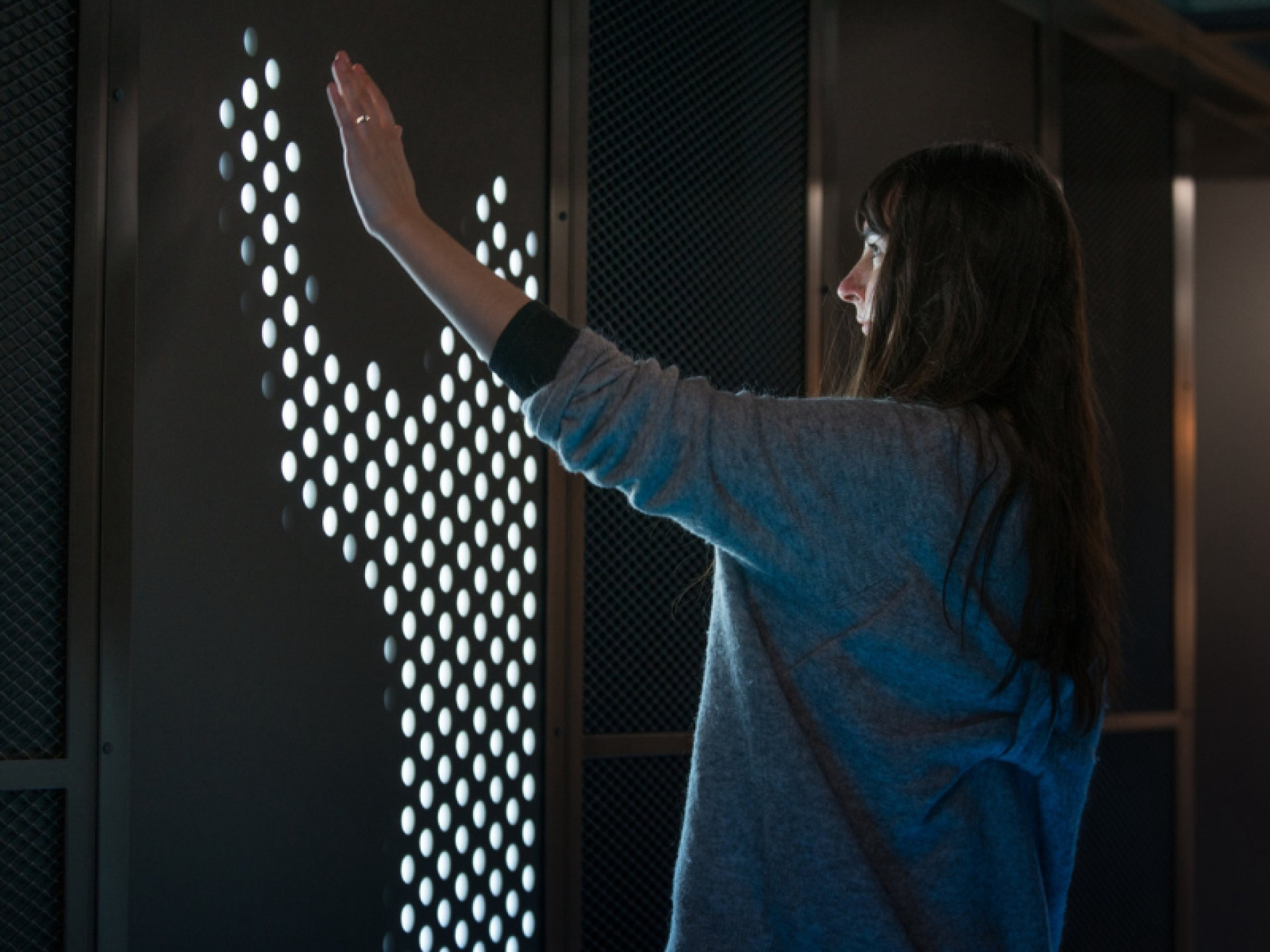 A woman interacts with a responsive digital installation at the Workspace Design Show in London, showcasing innovative workplace design.
