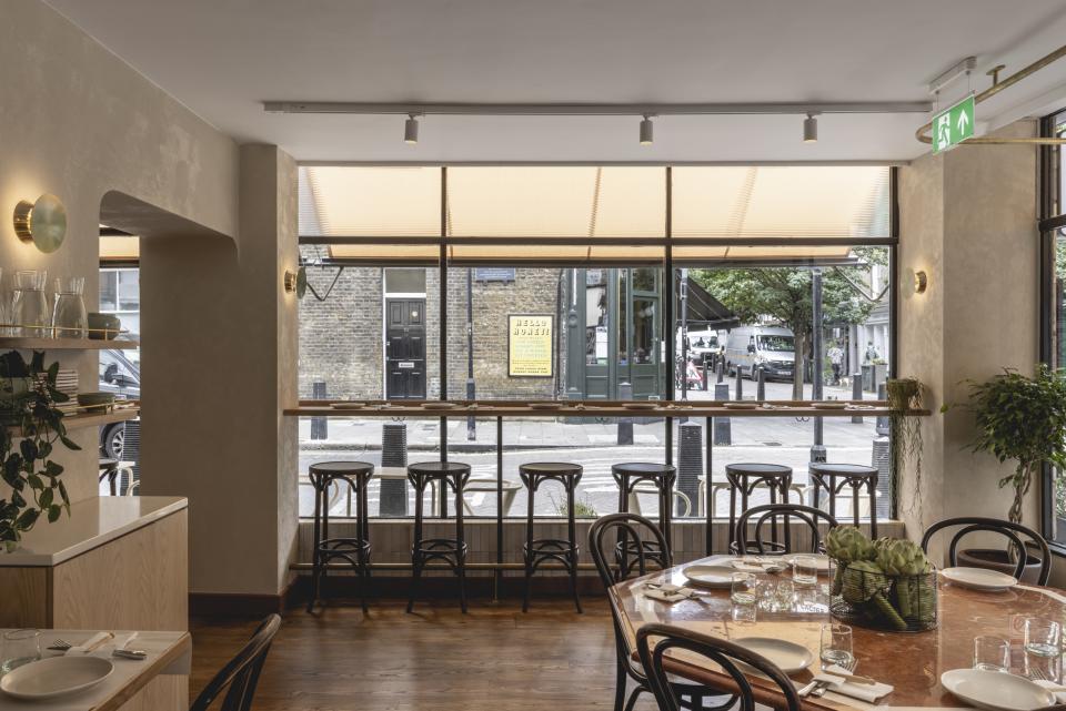 Elegant interior of Honey & Co restaurant in Bloomsbury, featuring wooden furniture, large windows, and a welcoming atmosphere.