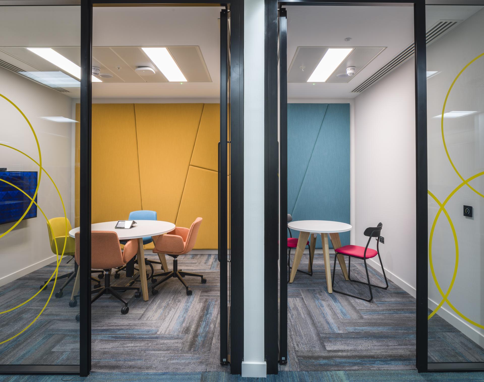 Modern office space showcasing two collaborative meeting rooms with vibrant colored walls and contemporary furniture design.