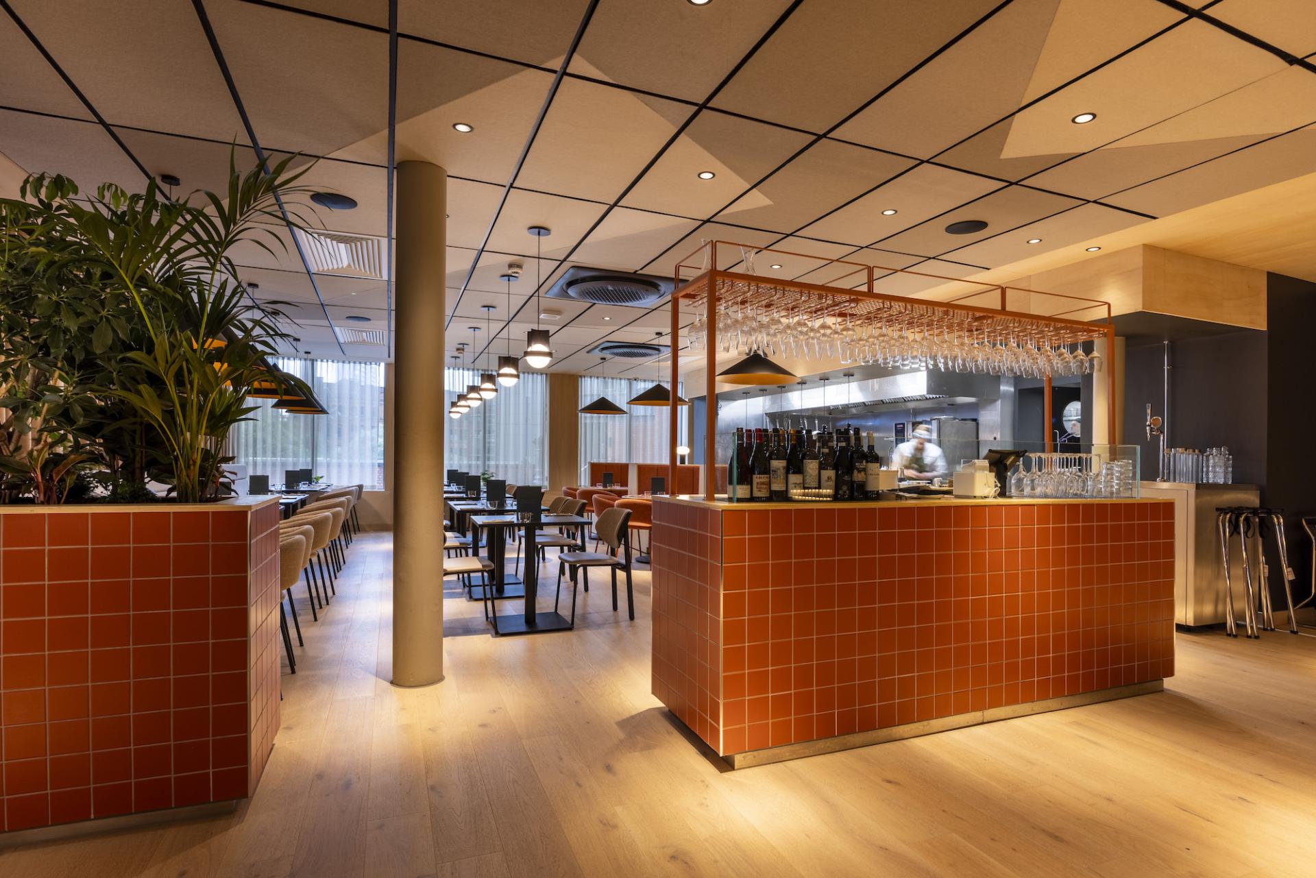 Modern restaurant interior featuring a stylish bar area with plants, wood flooring, and sophisticated lighting.