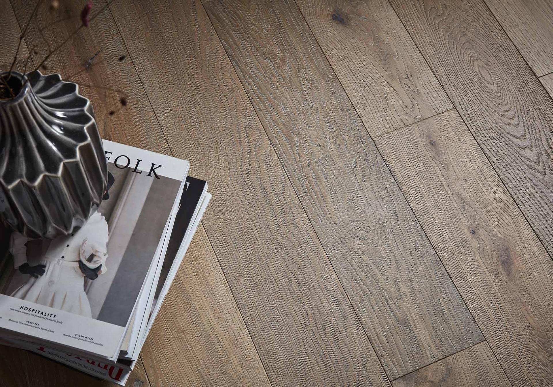 Elegant ceramic vase on top of magazines, resting on warm-toned wooden flooring, reflecting modern interior design aesthetics.
