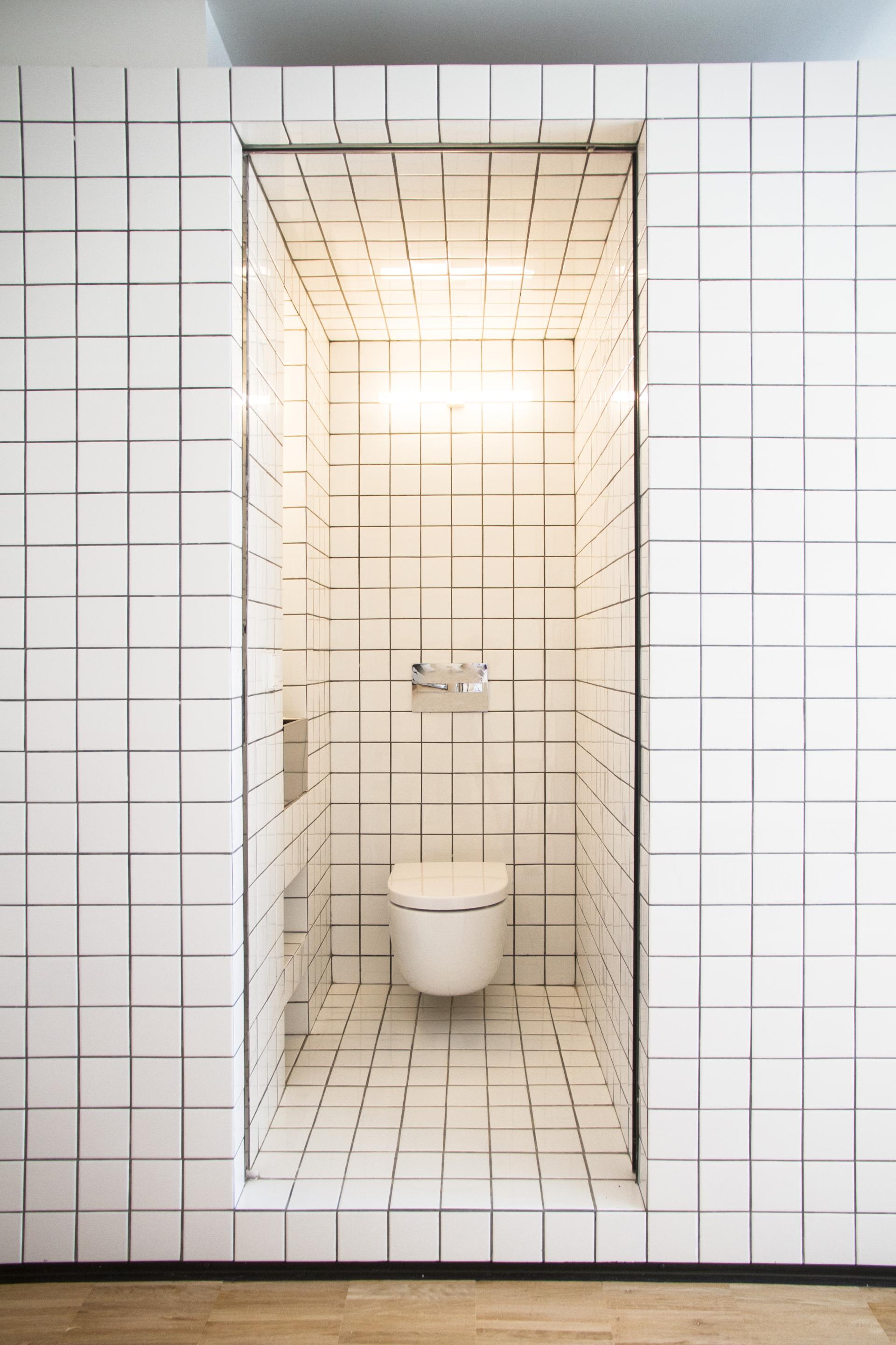 Minimalist bathroom design featuring white ceramic tiles with black grid pattern and modern toilet installation.