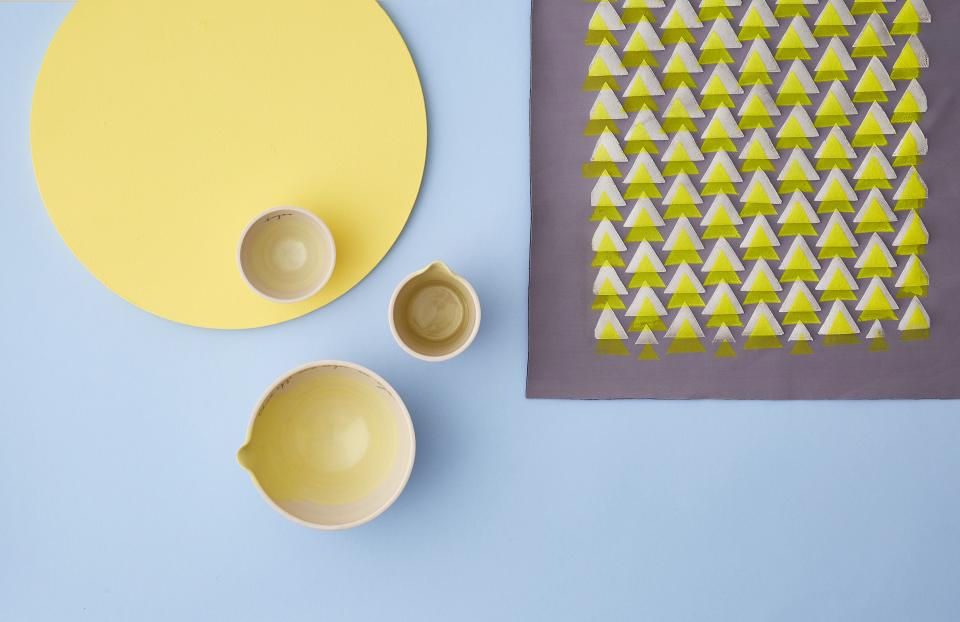 Colorful ceramic bowls on a pastel blue background, with a modern yellow geometric placemat and artistic textile design.