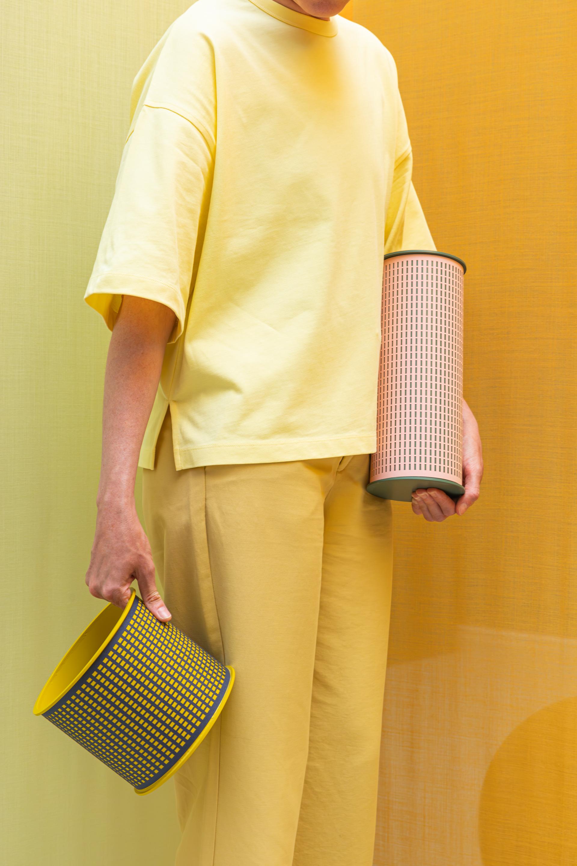 A person in a yellow outfit holds two modern, bio-based containers against a warm, textured backdrop.
