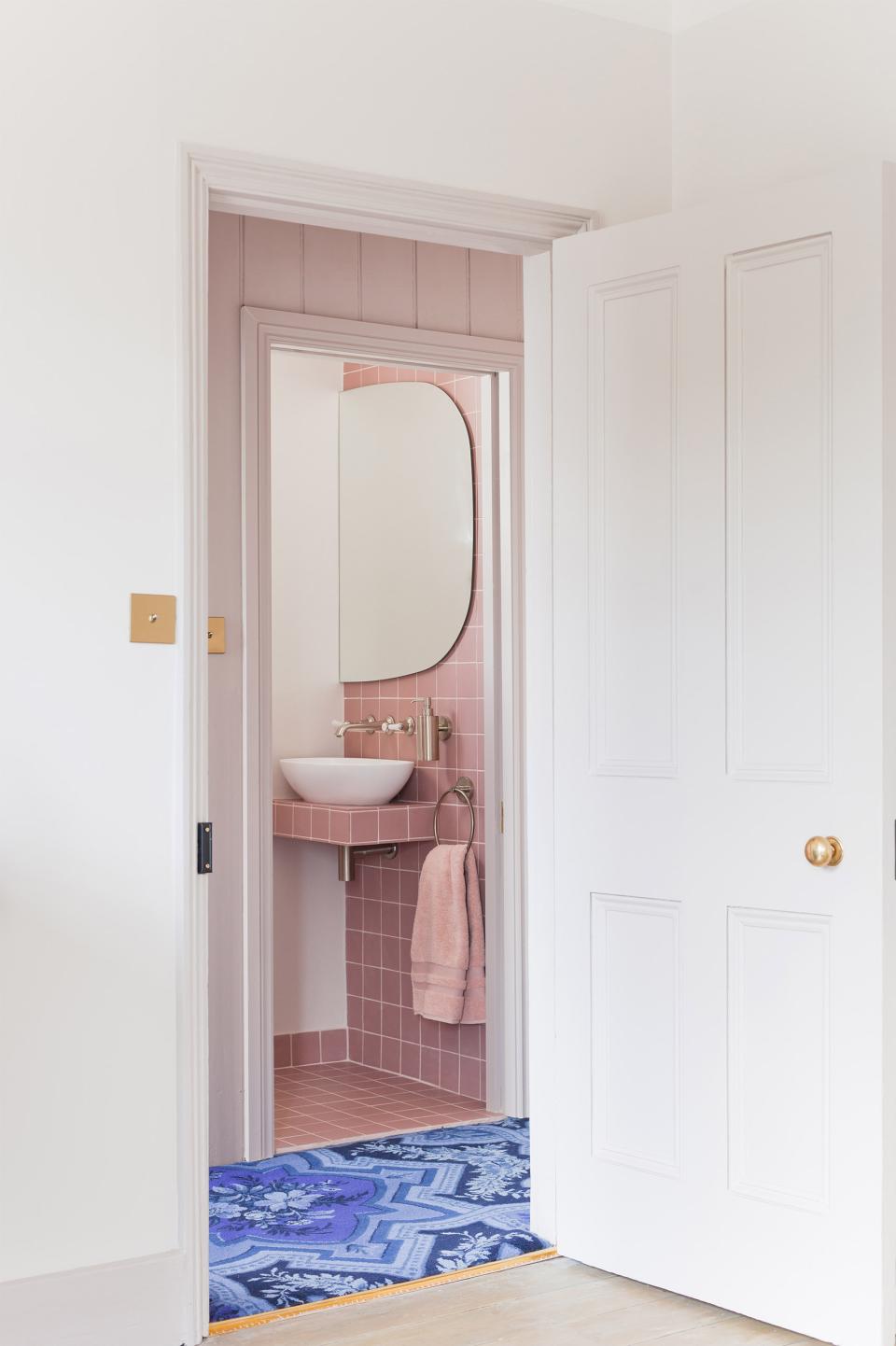 Stylish entrance to a pink-themed bathroom featuring modern fixtures, a circular mirror, and a decorative blue rug.