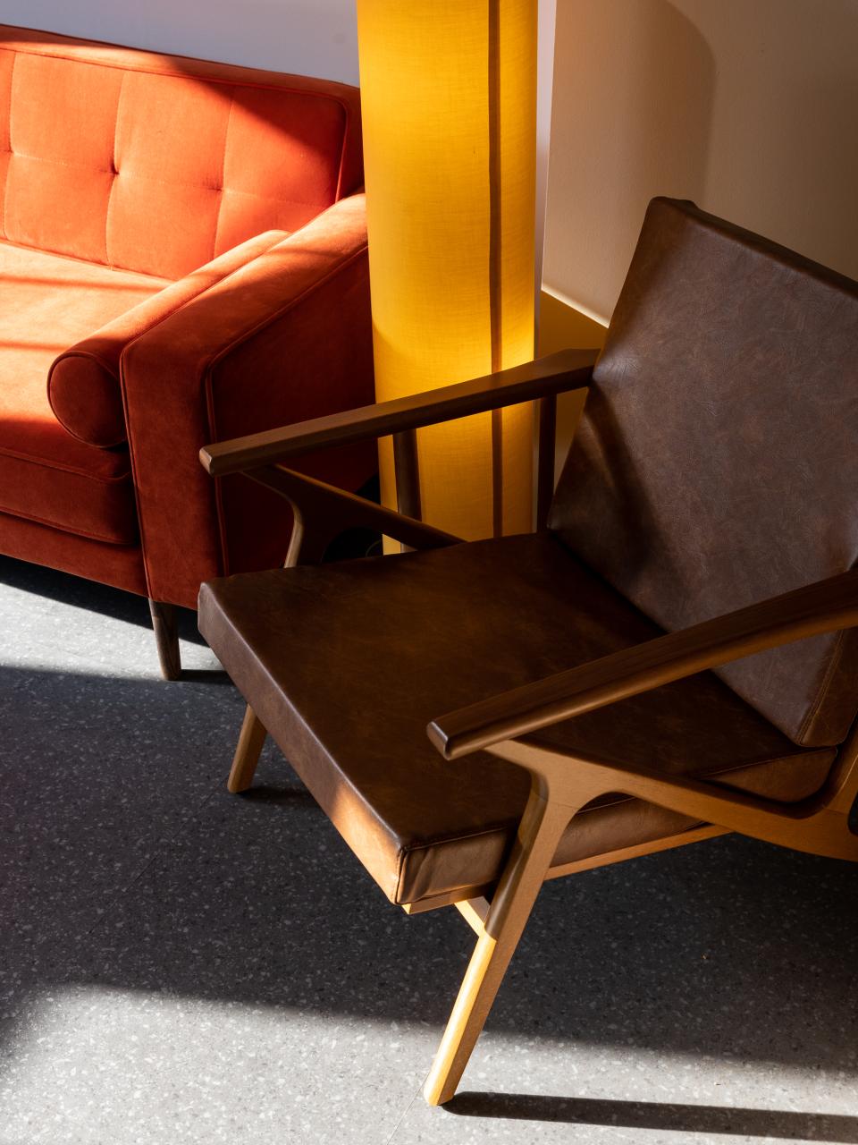 Stylish seating arrangement featuring a vintage brown chair and a vibrant red couch, surrounded by warm light.
