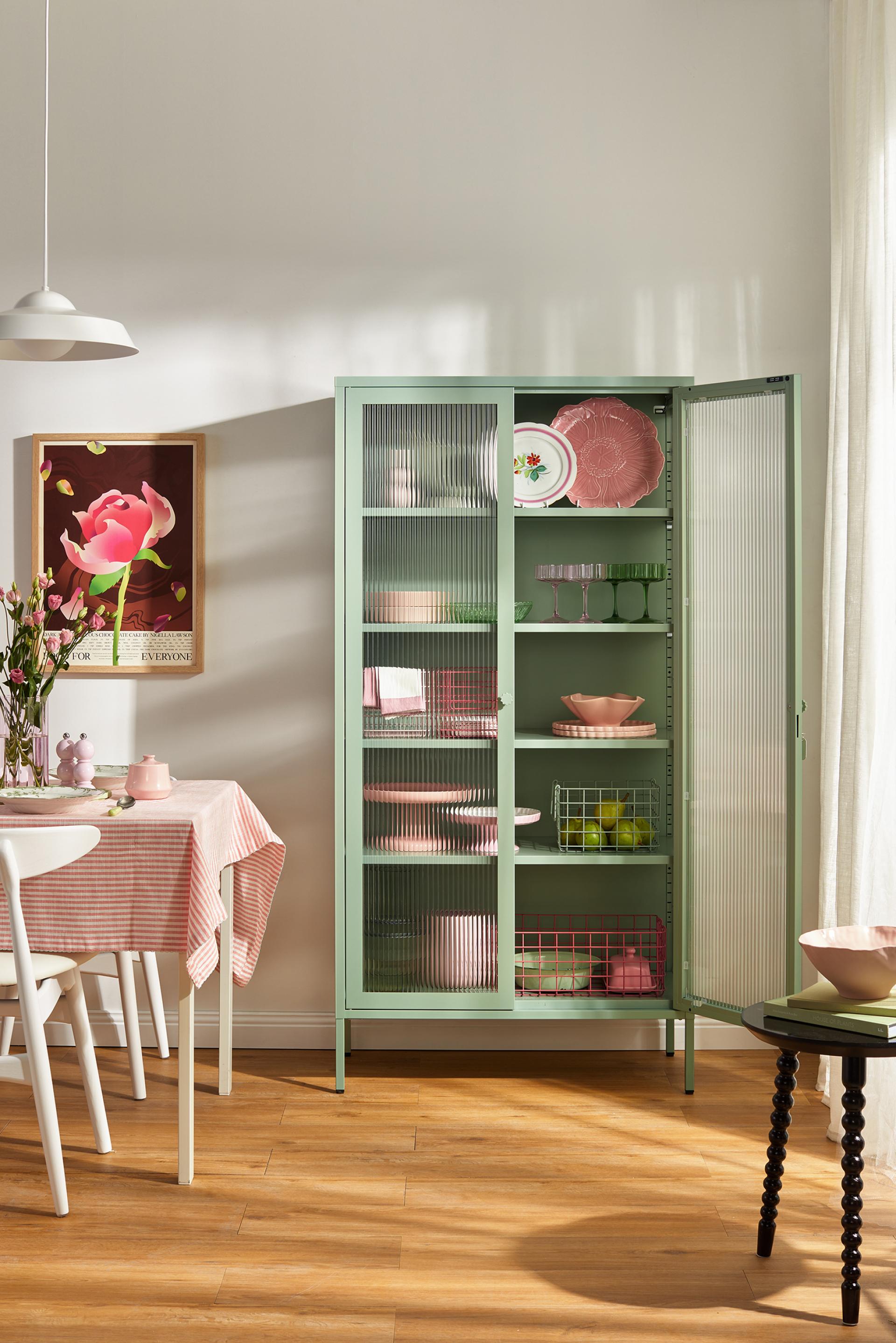 Stylish green glass cabinet displaying colorful plates and glassware in a contemporary dining setting.