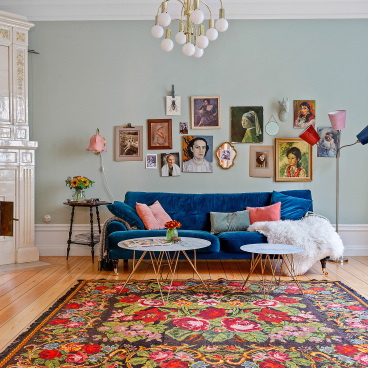 Cozy Scandinavian living room featuring a blue velvet sofa, floral rug, and an array of art on the walls.