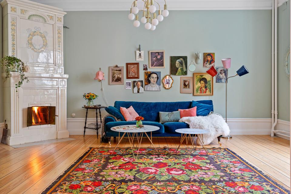 Cozy Scandinavian living room featuring a blue velvet sofa, floral rug, and an array of art on the walls.