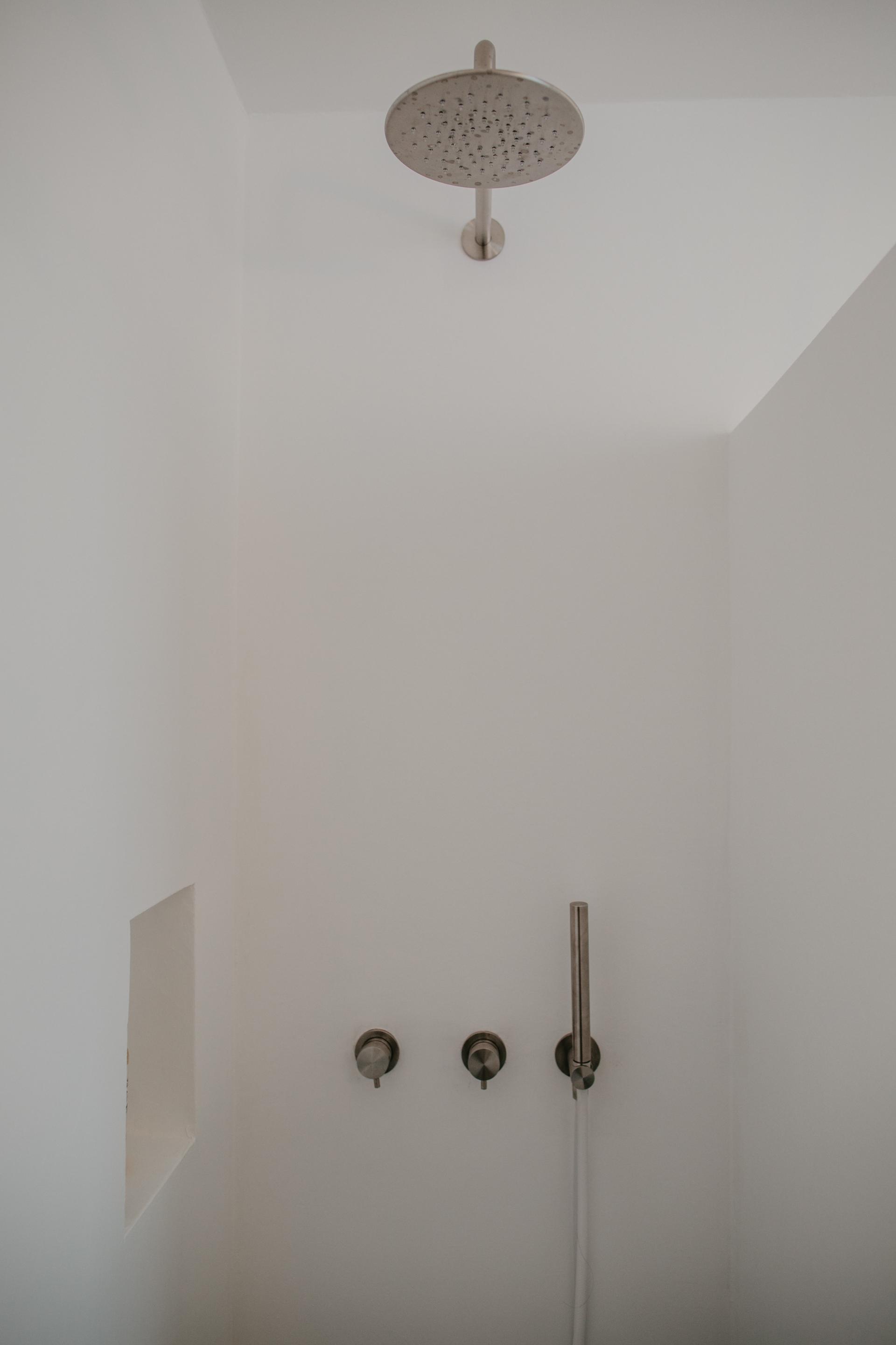Stylish showerhead and sleek control knobs in a minimalist bathroom, highlighting Quadrodesign's Source collection.