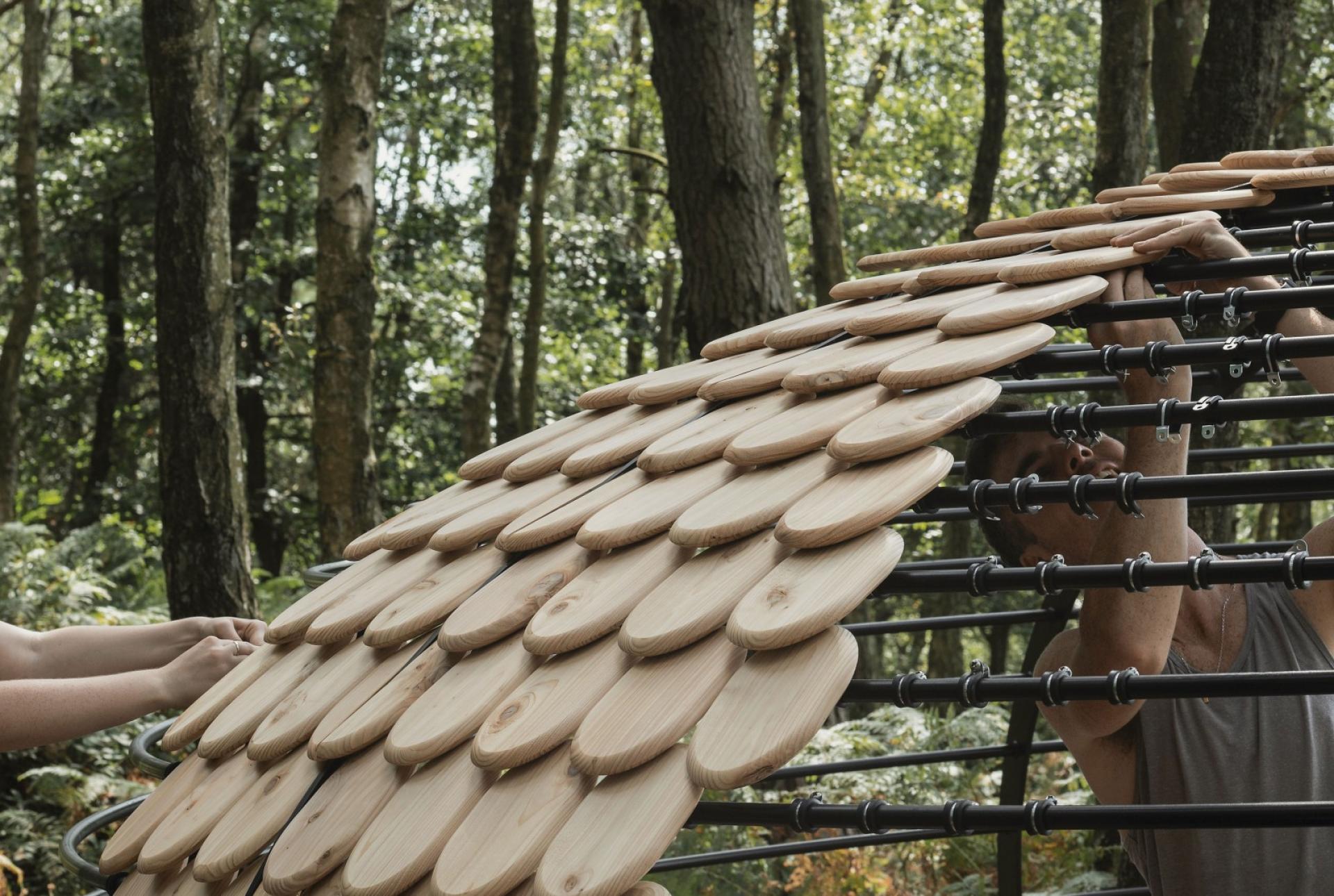Workers assembling the wooden roof of the Perspectives pavilion amidst the lush greenery of Winterfold Forest, Surrey.