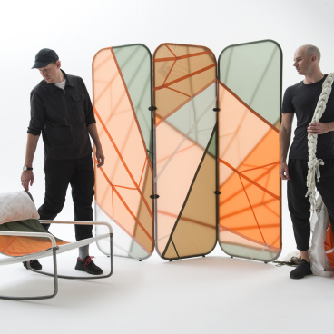 Two designers interact with innovative furniture made from recycled parachute material and steel frames, showcasing unique structure and form.