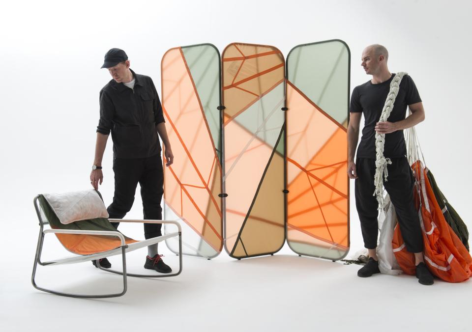Two designers interact with innovative furniture made from recycled parachute material and steel frames, showcasing unique structure and form.