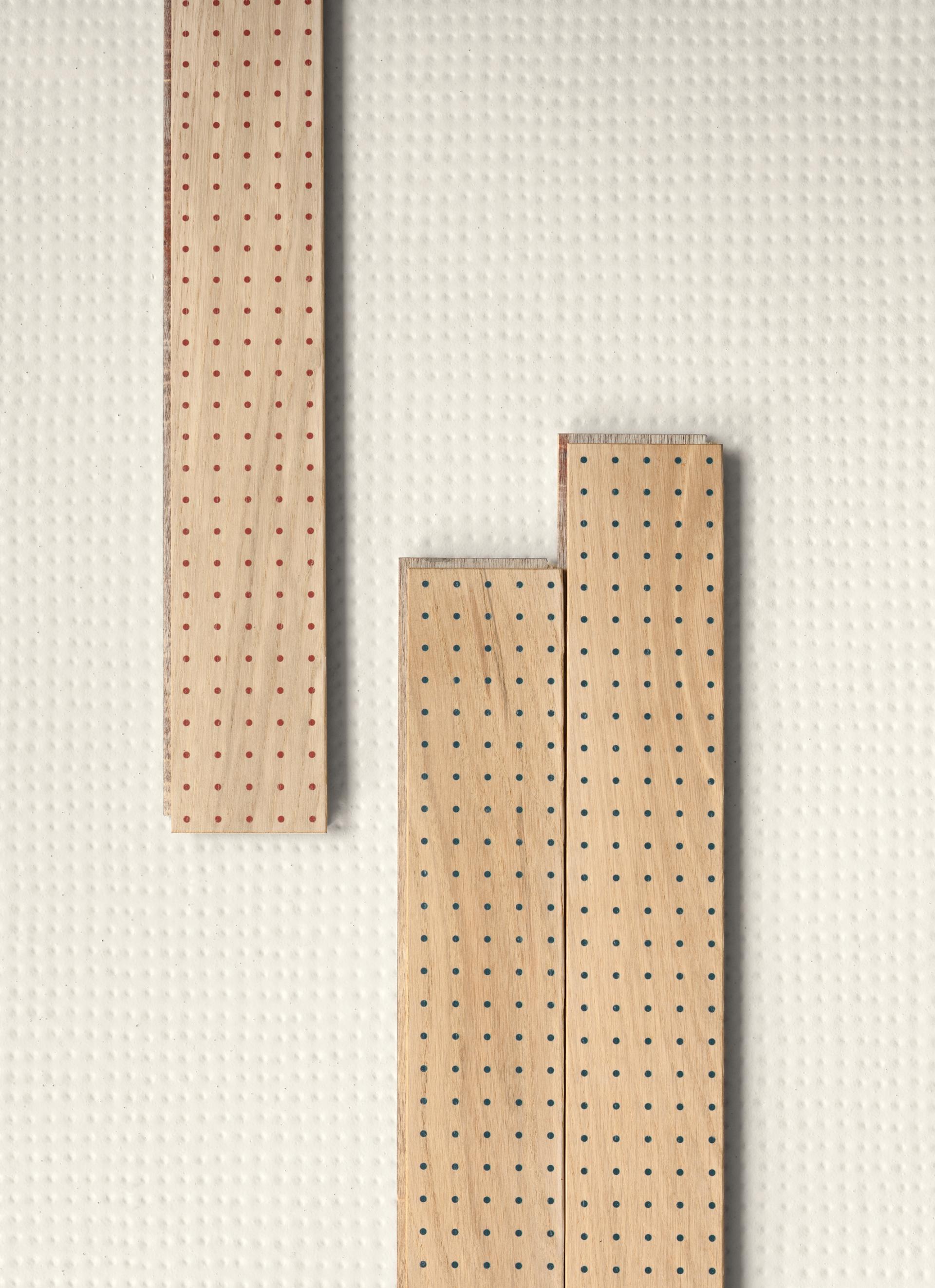 Wooden panels with red and blue perforations arranged artistically on a textured white background, representing Mutina and Studio Bouroullec's collaboration.