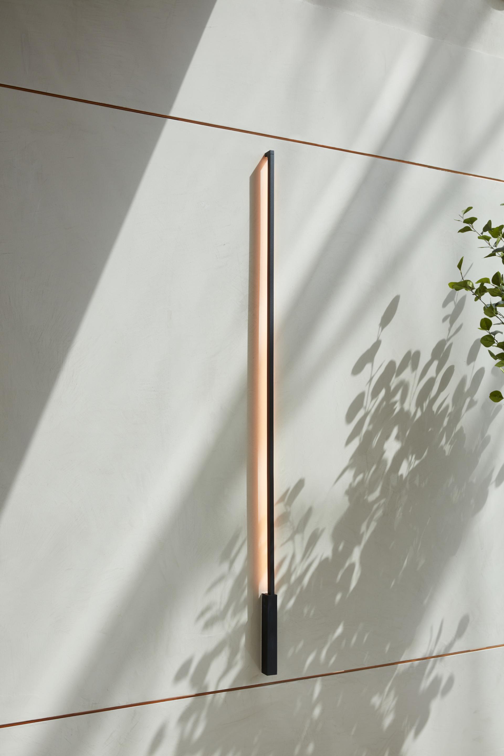 Sleek vertical light fixture casts elegant shadows on textured wall in modern Dubai Internet City office design by Roar.