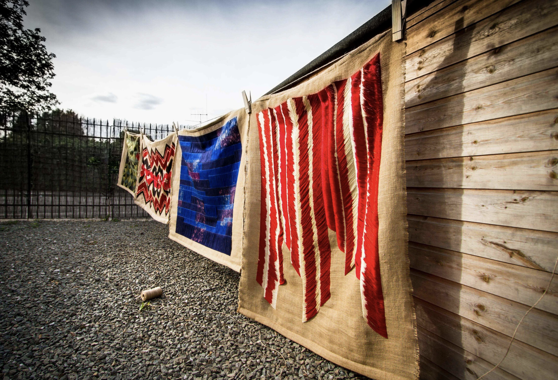 Large-scale contemporary wall hangings showcasing vibrant Slovakian embroidery techniques displayed outdoors against a wooden backdrop.