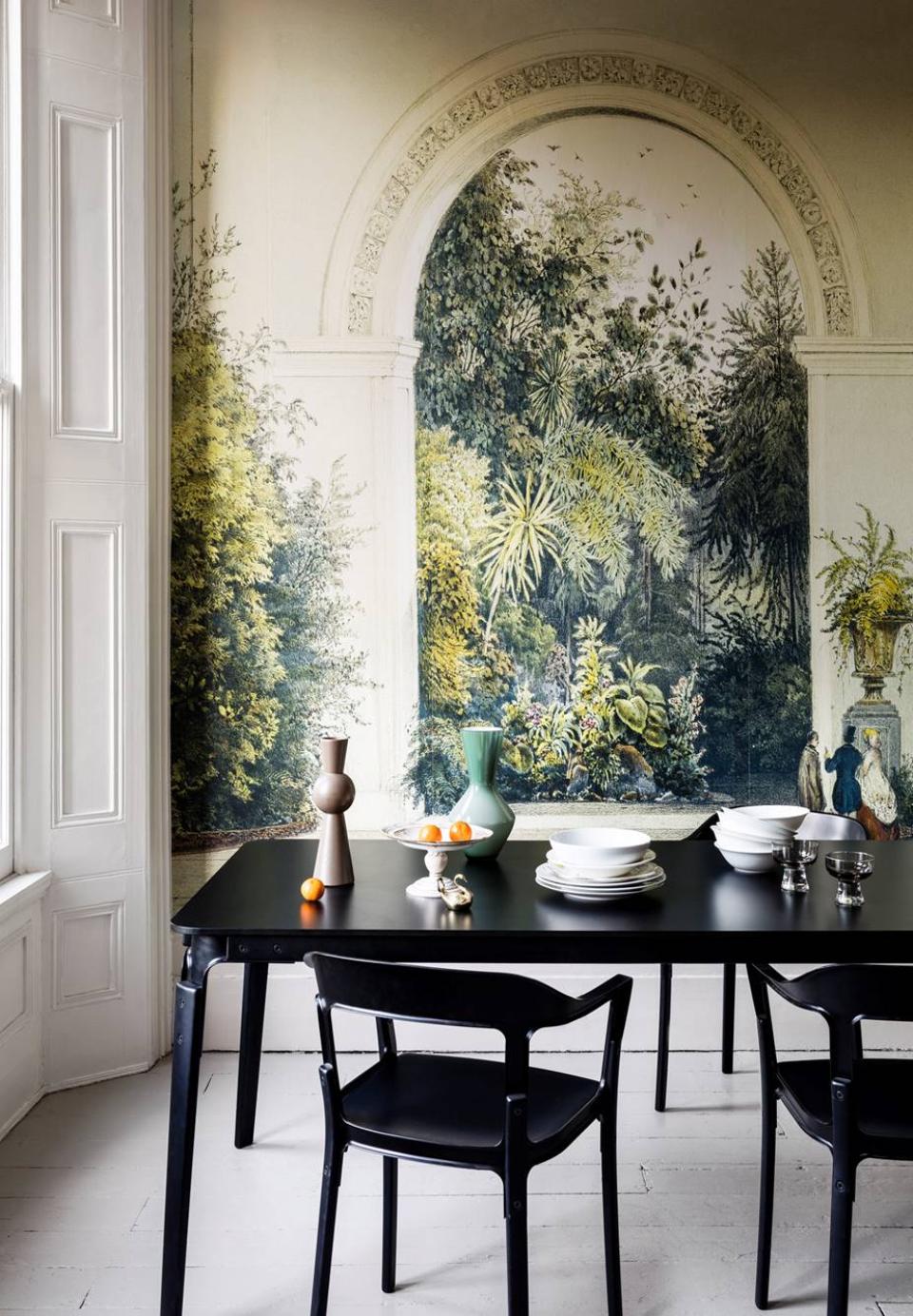 Elegant dining table set against a botanical mural, featuring decorative vases and plates, enhancing a green-themed ambience.