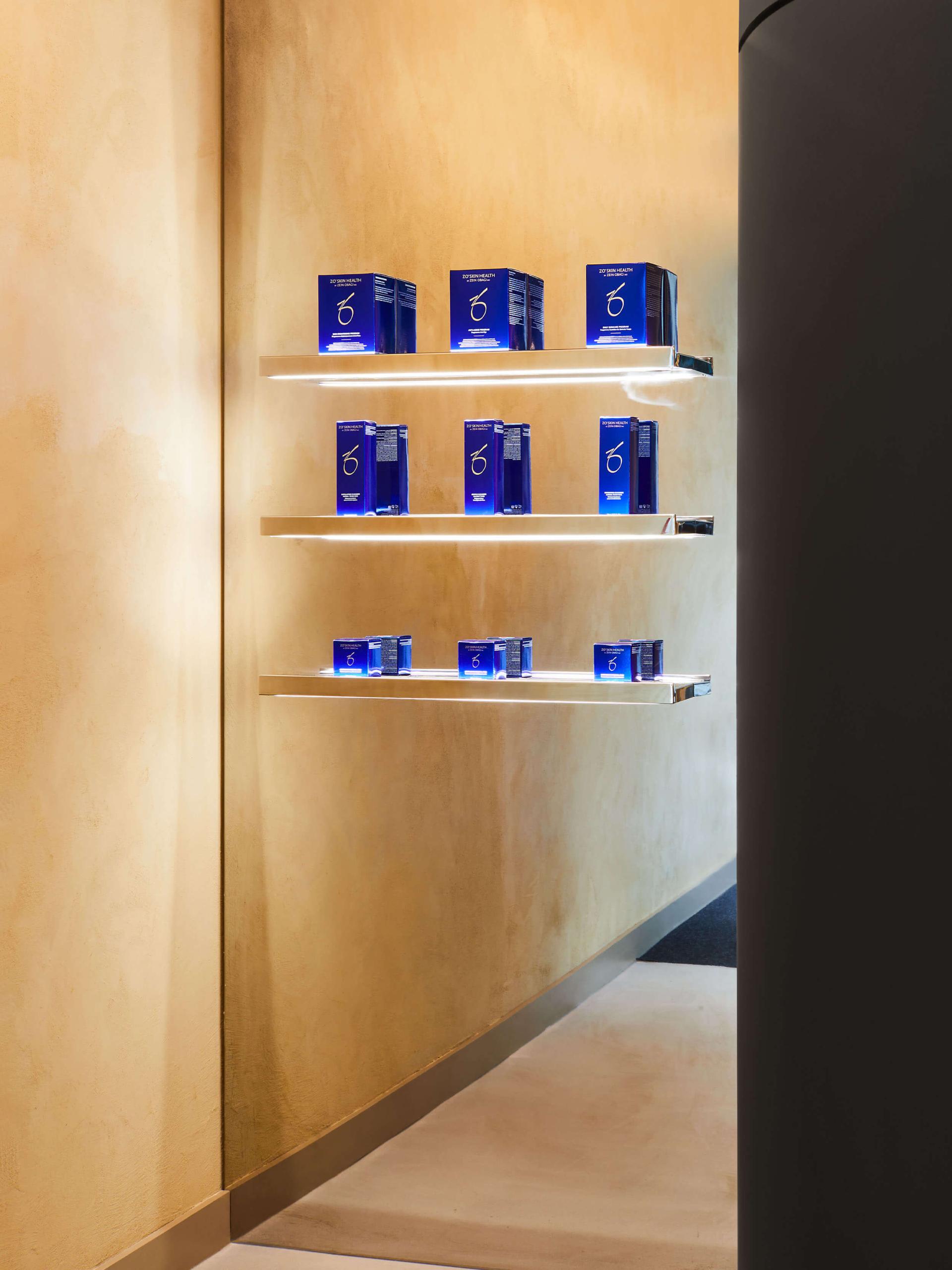 Shelves displaying elegantly packaged skincare products against a warm, neutral-toned wall in a modern healthcare setting.