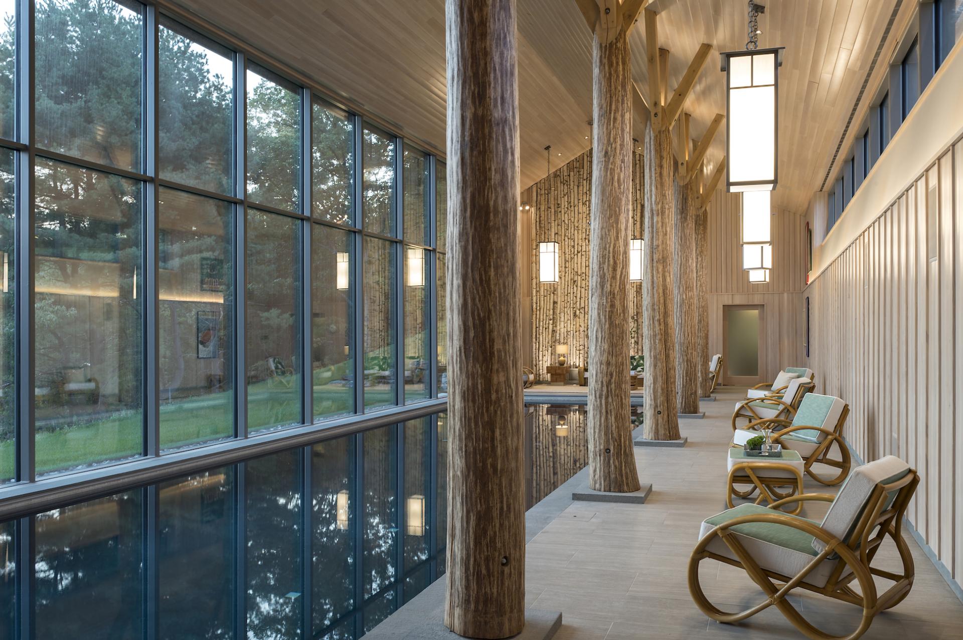 Tranquil interior of Lazy Bear Pool House featuring tall windows, wooden columns, and modern lounge chairs overlooking a serene pool.