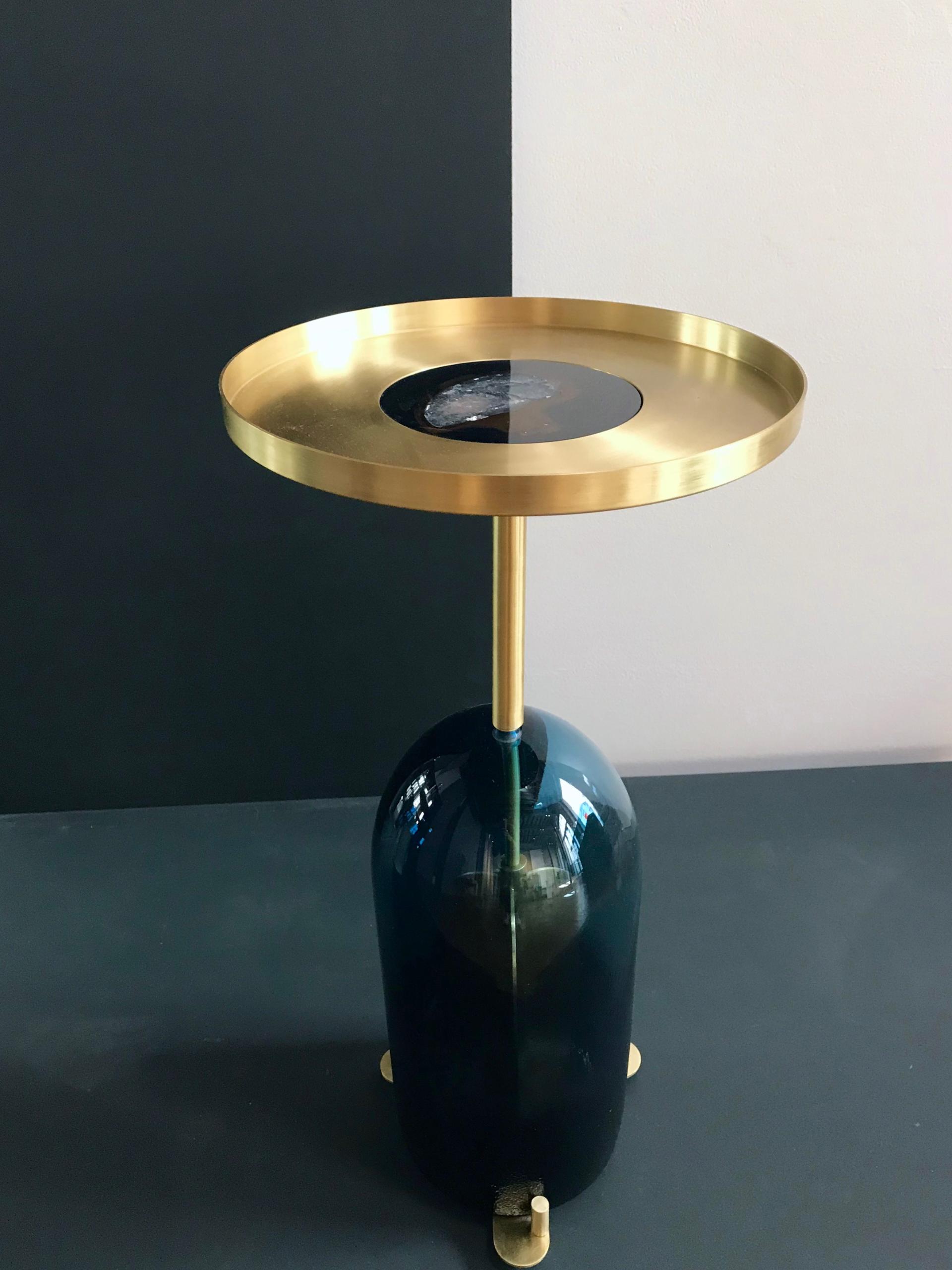 Modern brass and glass side table displayed against minimalist black and white backdrop at Paris Design Week.