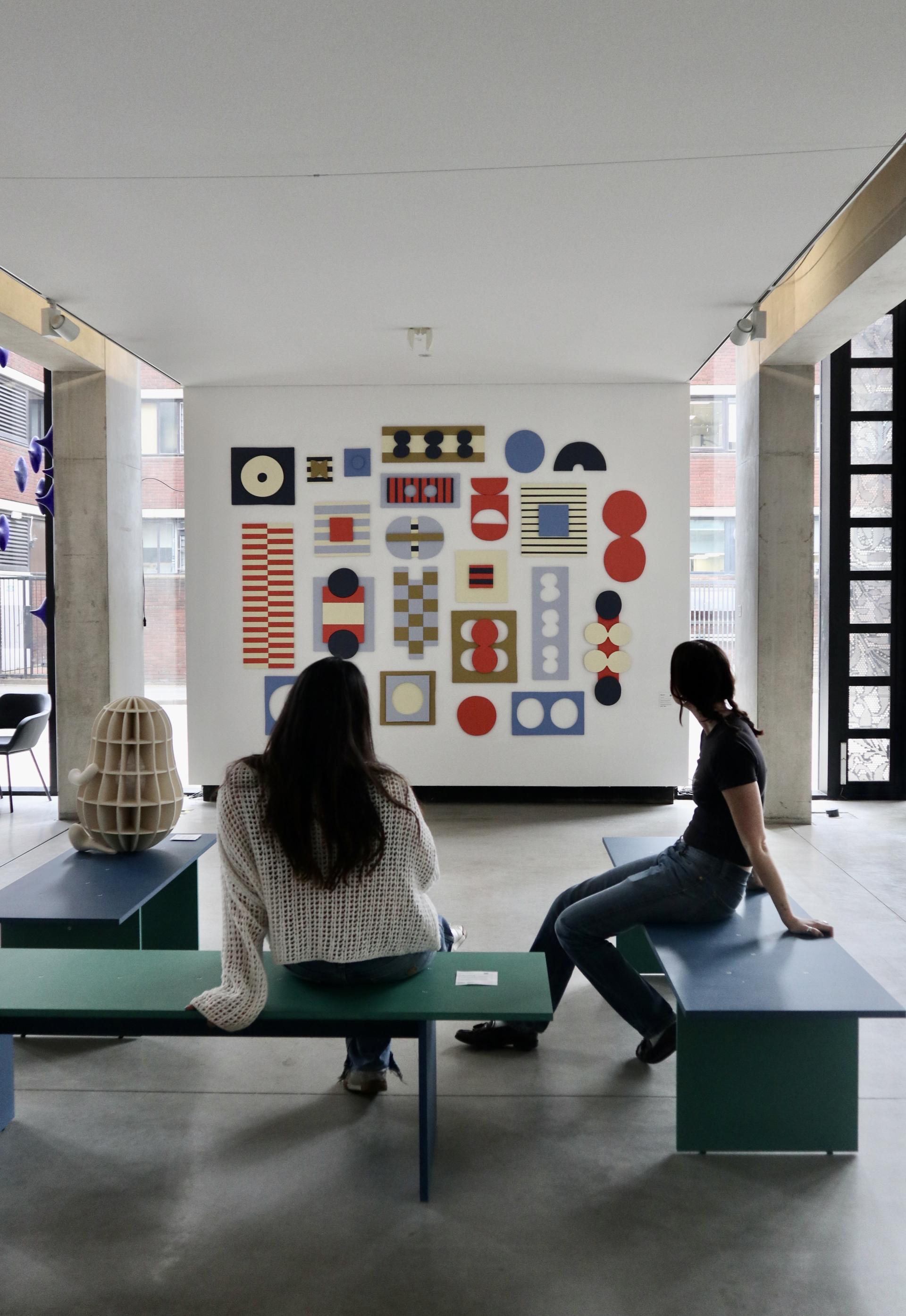 Visitors admire colorful artwork displayed on a gallery wall at the Manchester School of Art.