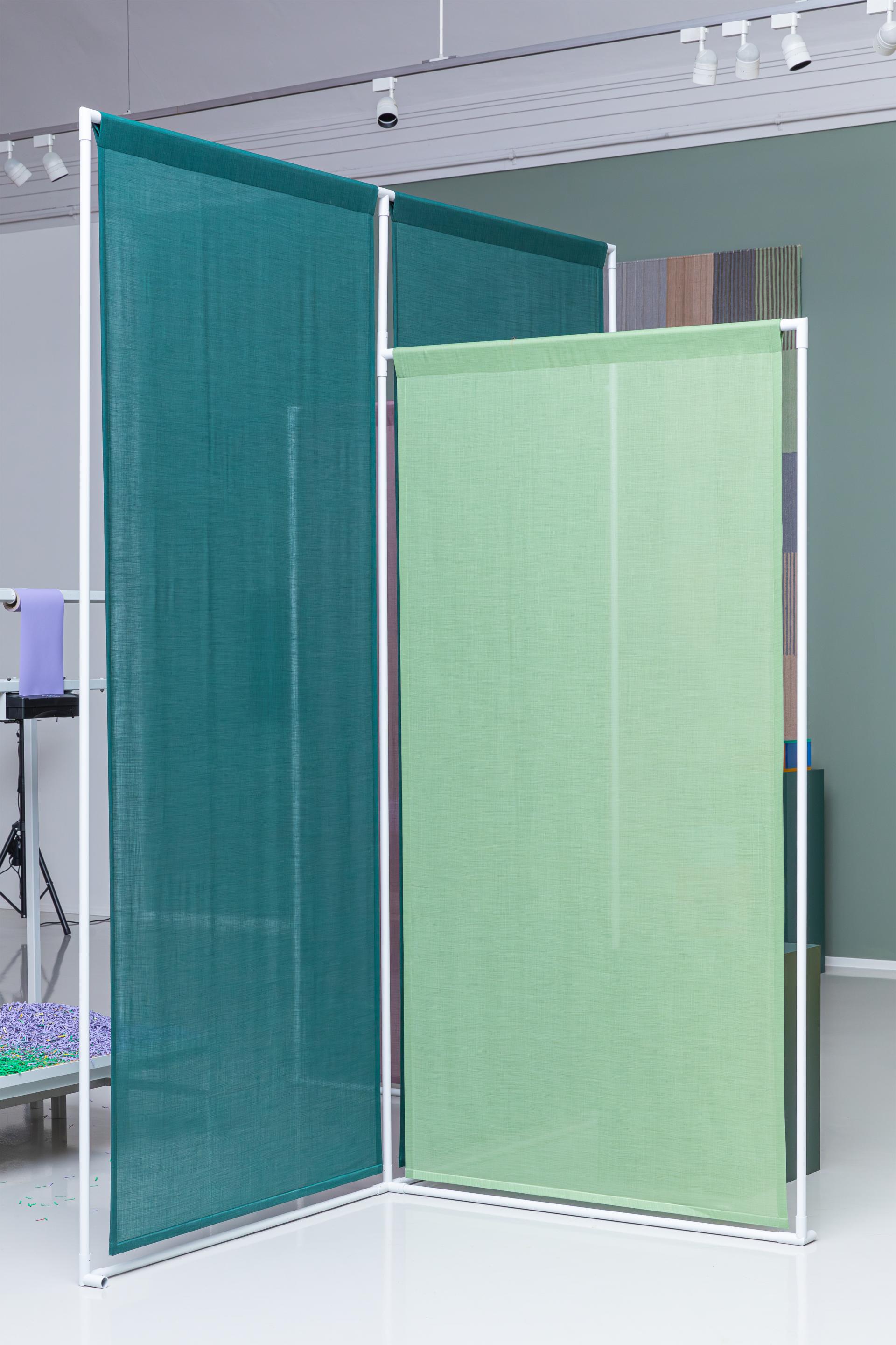 Textile panels in green and teal showcase bio-based color palettes in a minimalist exhibition space.