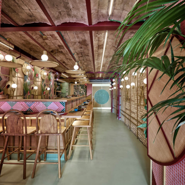 Modern tropical sushi restaurant interior featuring vibrant decor, wooden seating, and lush greenery designed by Masquespacio in Valencia.