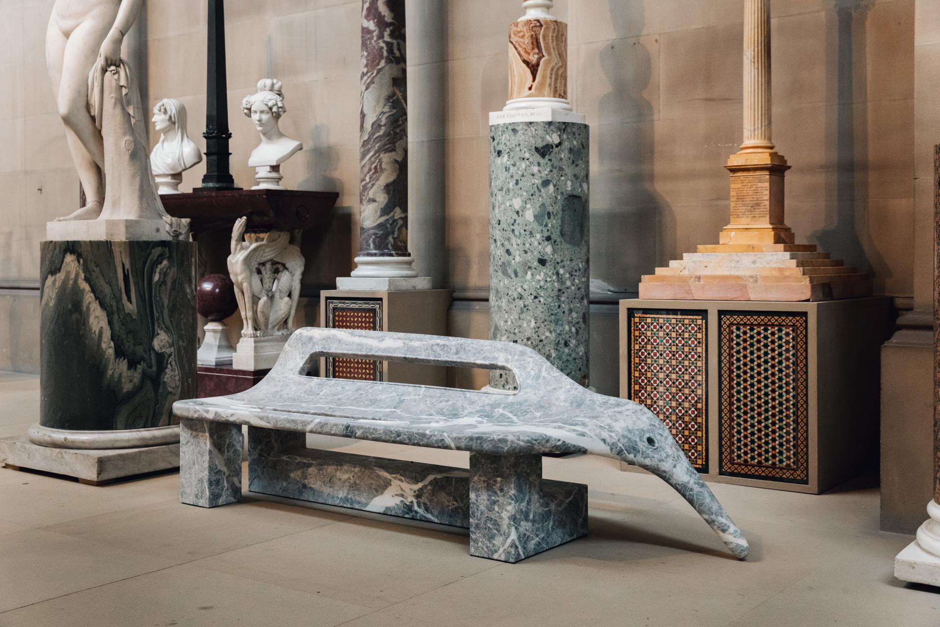 Sculptural marble bench in Chatsworth House amidst classical statues and decorative columns, highlighting its heritage and artistry.