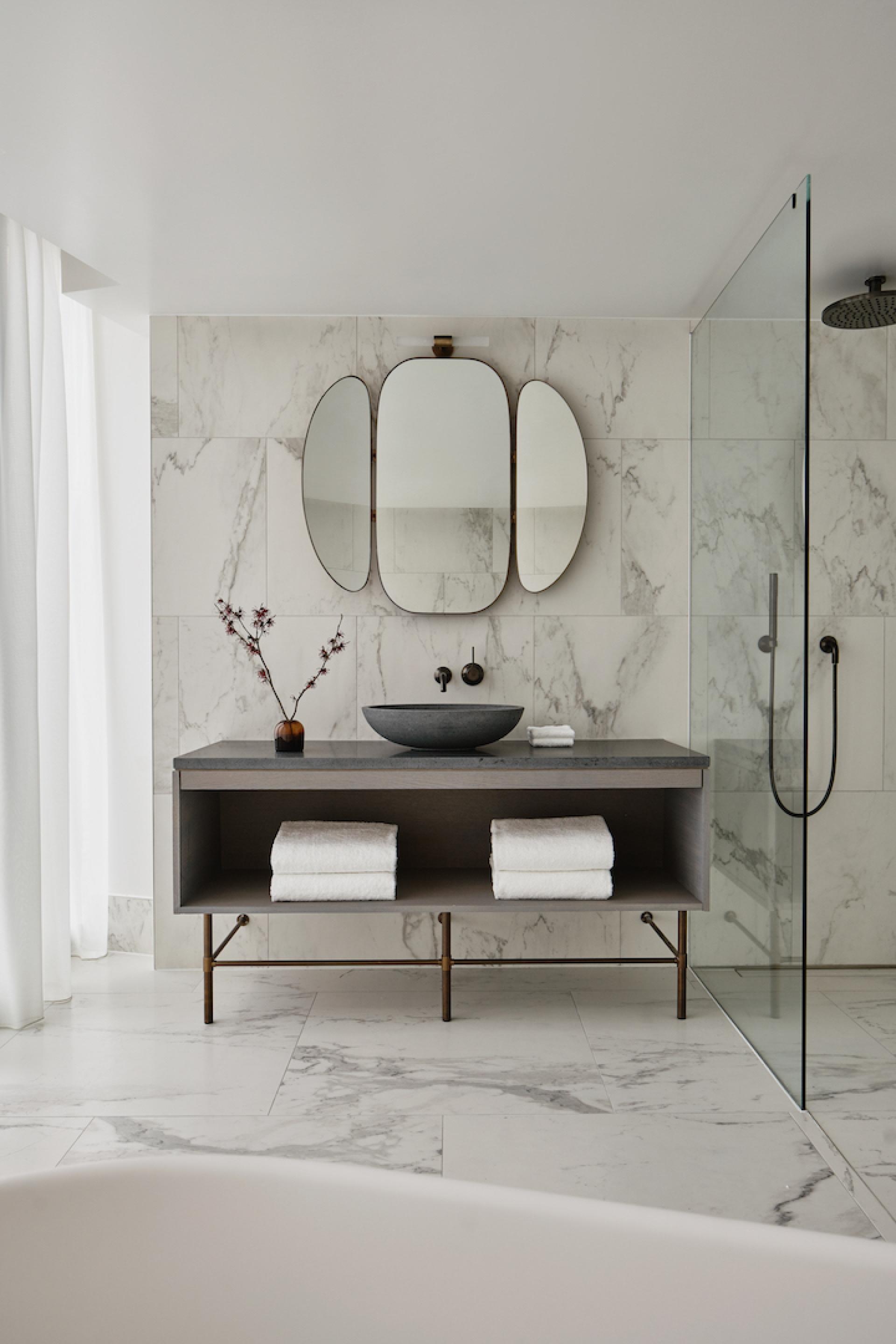 Elegant bathroom design featuring a marble wall, modern basin, decorative mirror, and neatly arranged towels.