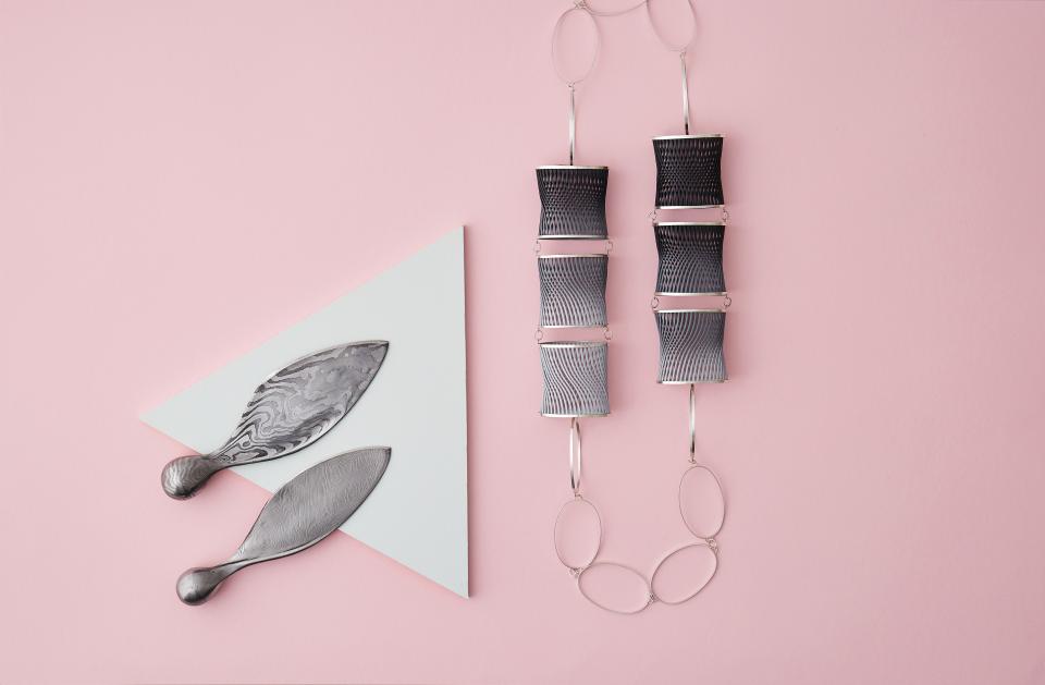 Contemporary metallic jewelry and sculptural artifacts displayed artfully on a pink background, highlighting new design talent.