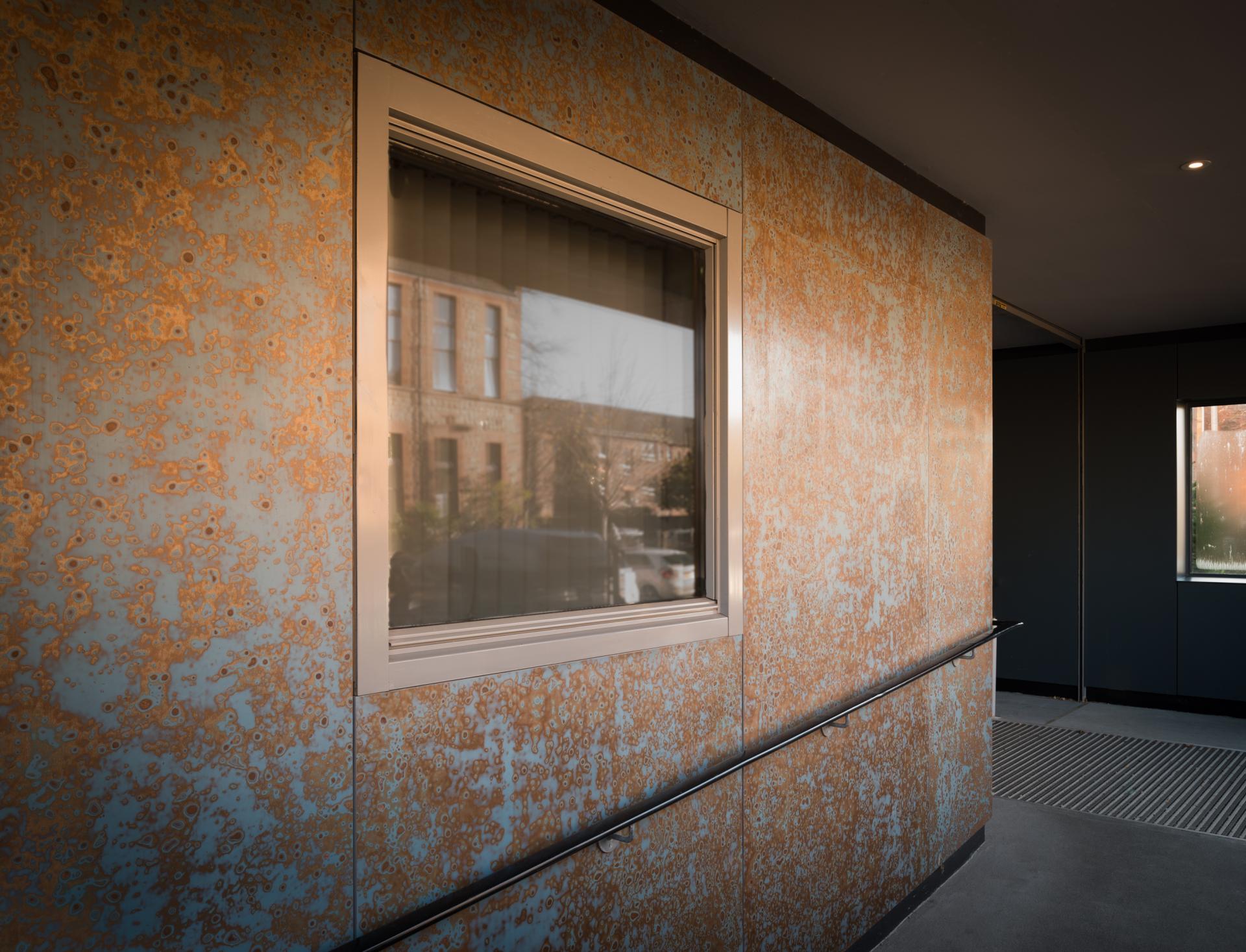Textured wall with a window reflecting urban surroundings, showcasing modern surface design influences inspired by Japanese lacquerware.
