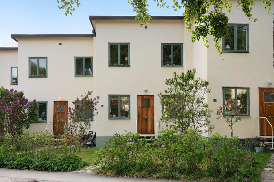 Row of Scandinavian homes with modern design, featuring green windows and blooming gardens, typical of Swedish architecture.