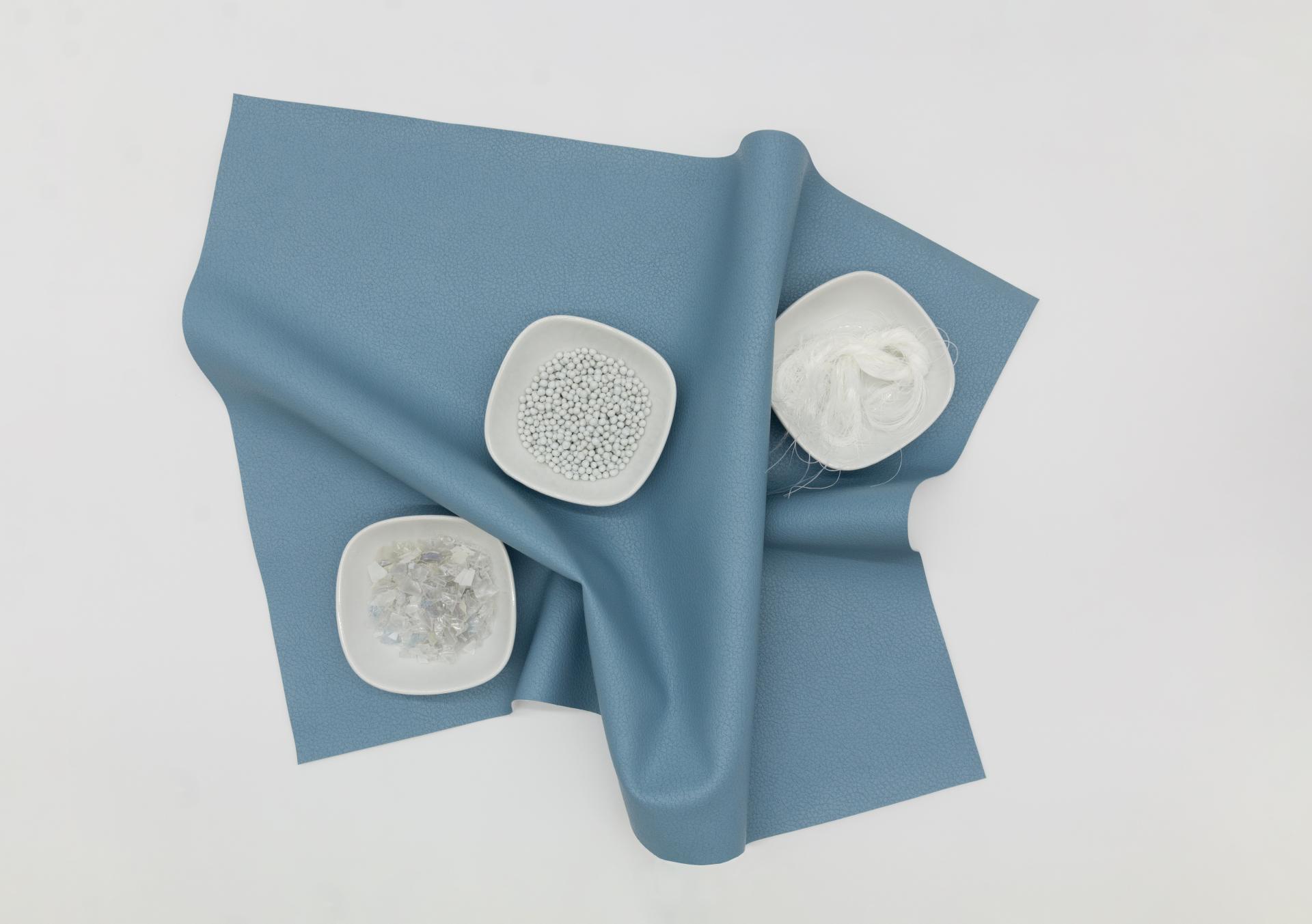 Recycled fabric laid out with small bowls of plastic pellets, flakes, and fibers, showcasing sustainable material use.