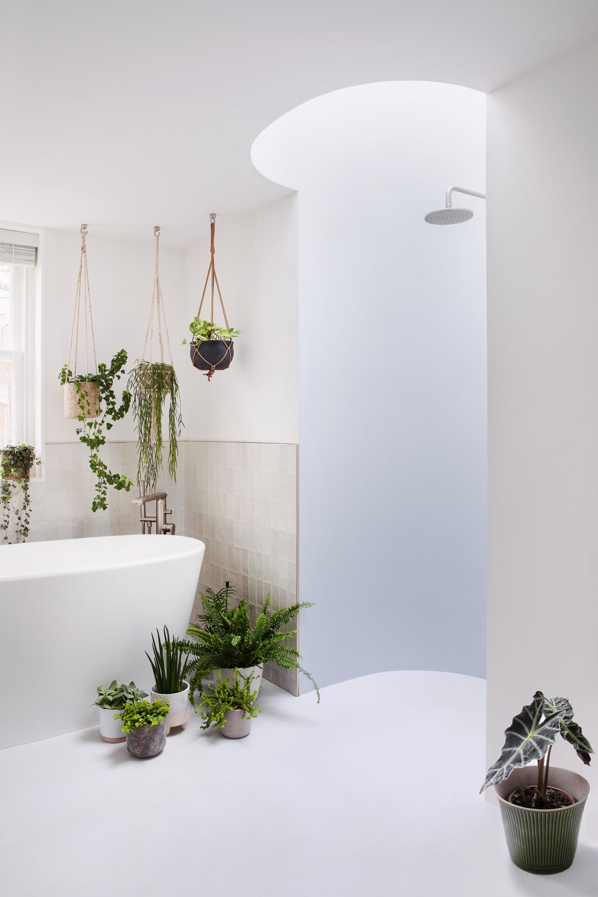 Modern bathroom featuring a freestanding tub, hanging plants, and natural light, showcasing sustainable design principles.