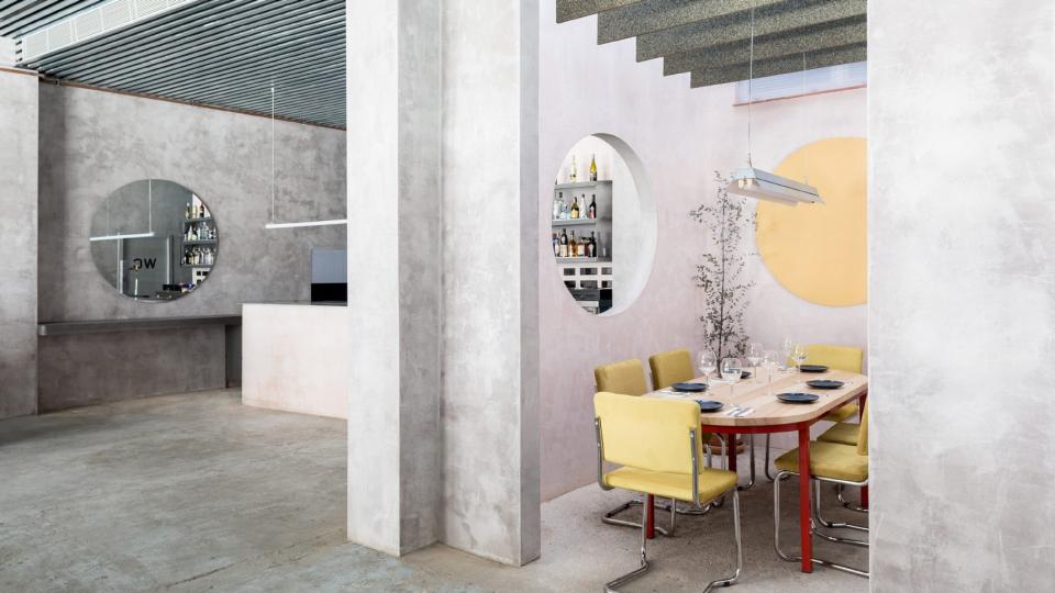 Contemporary Seville restaurant interior featuring concrete walls, colorful furniture, and elegant dining setup with table and chairs.