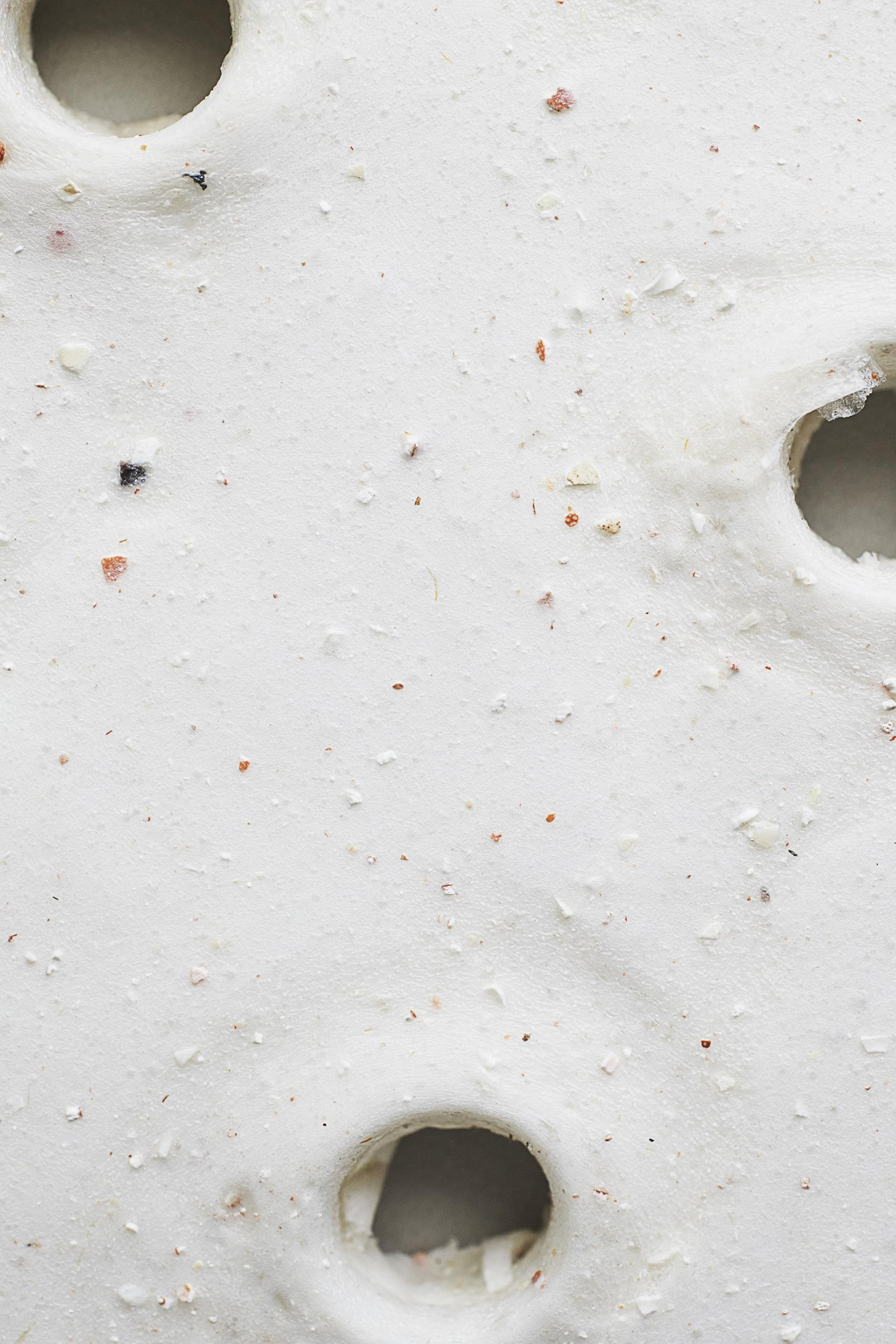 Textured white biomaterial surface featuring small flecks and circular holes, highlighting sustainable, waste-based product innovation for 2025.