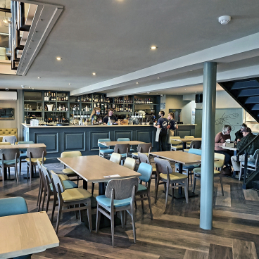 Modern restaurant interior featuring a bar, staff serving guests, and comfortable seating, highlighting the adaptability of hospitality spaces.