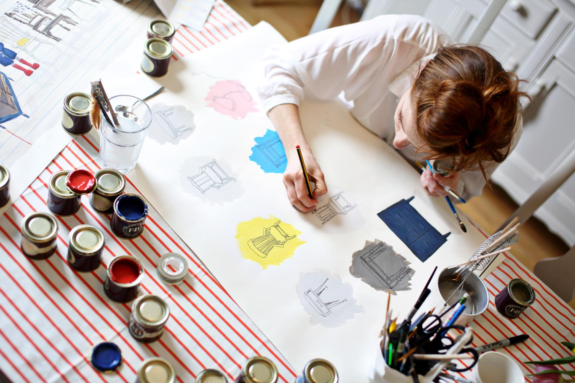 Artist painting furniture sketches with colorful swatches, highlighting trends in interior design at Farrow & Ball.