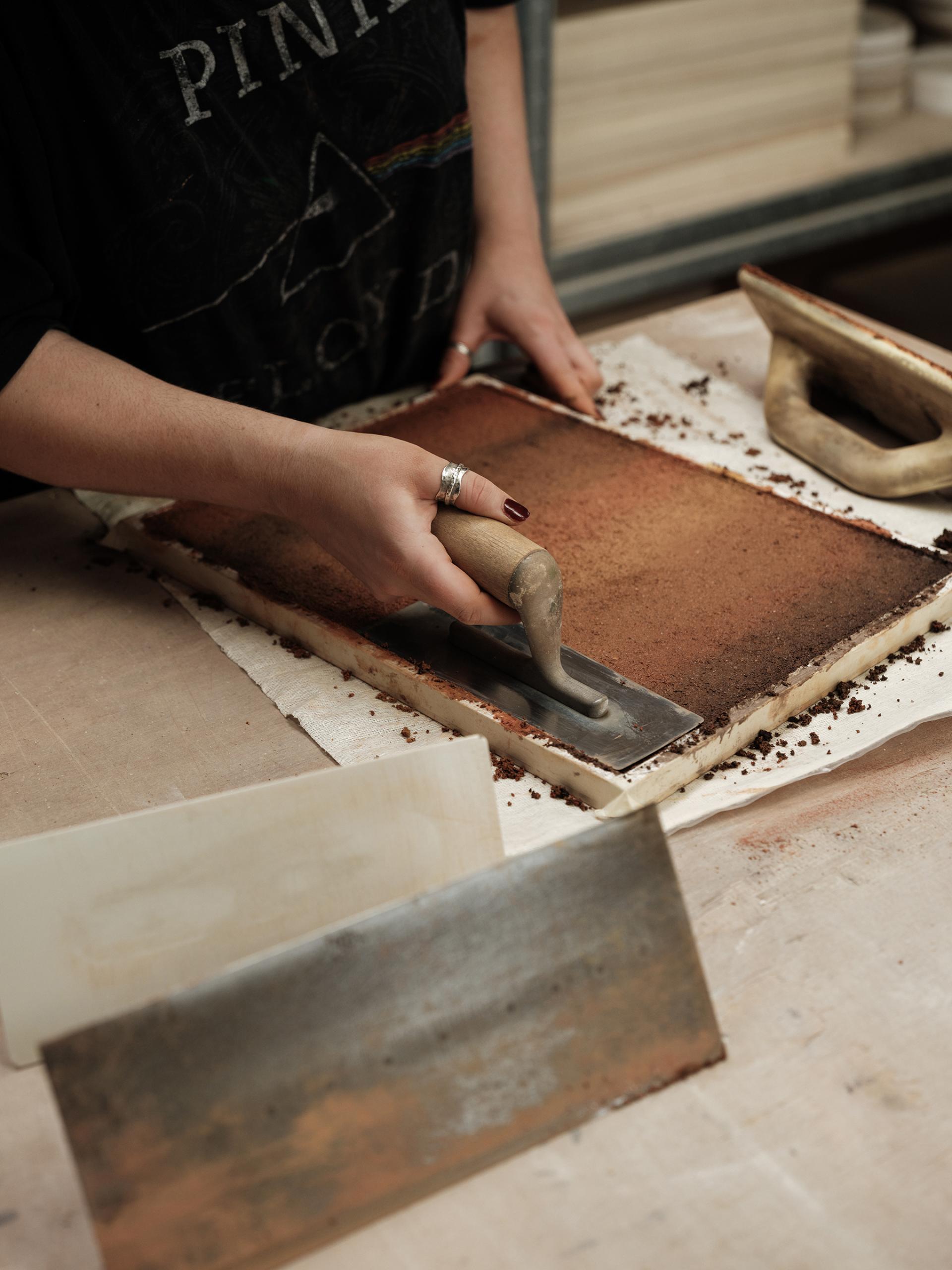 Craftsperson applying a low carbon wall finish using a trowel on a textured surface inspired by rammed earth.