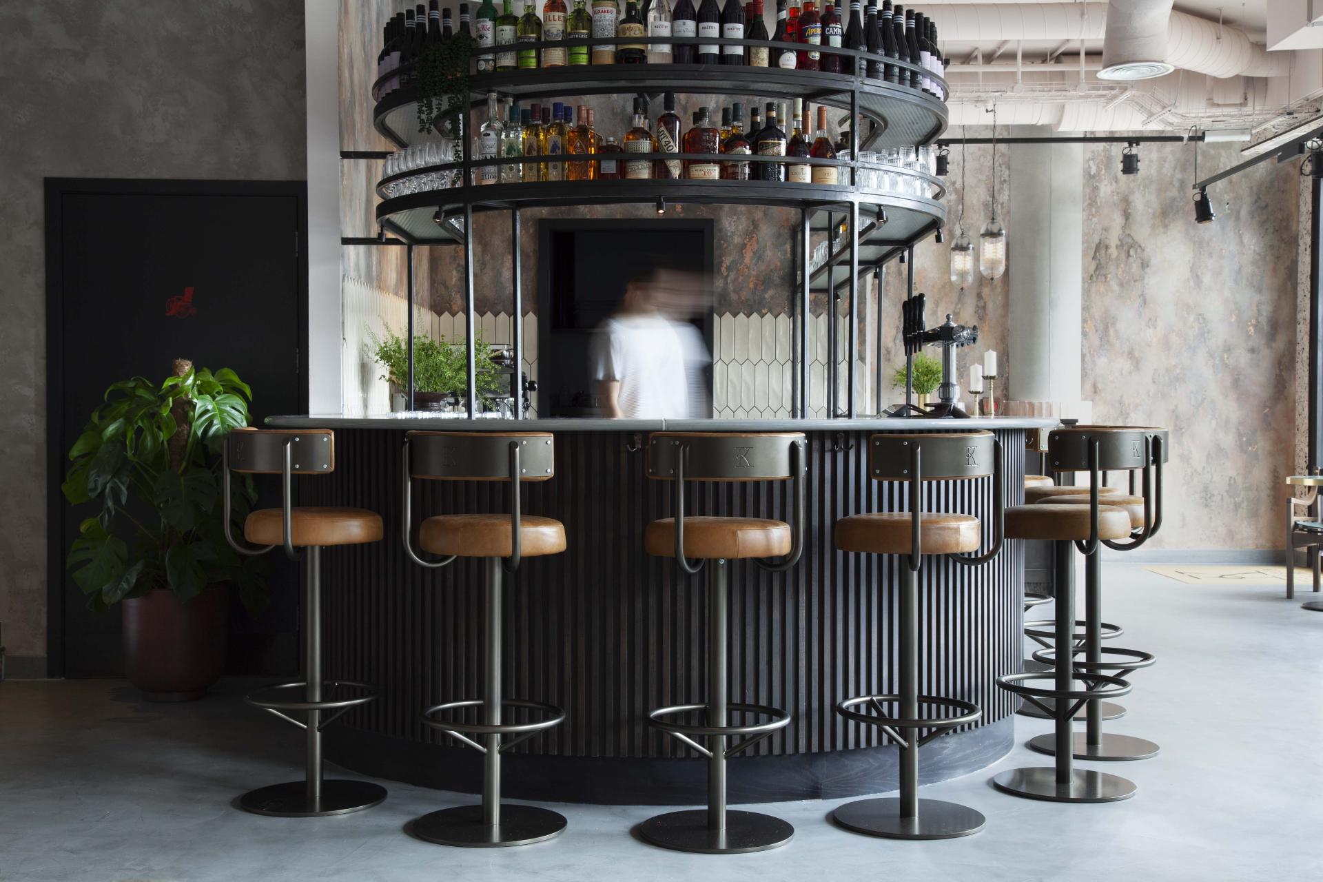Stylish bar area in Kricket restaurant, featuring circular shelving, modern stools, and a warm, inviting atmosphere.